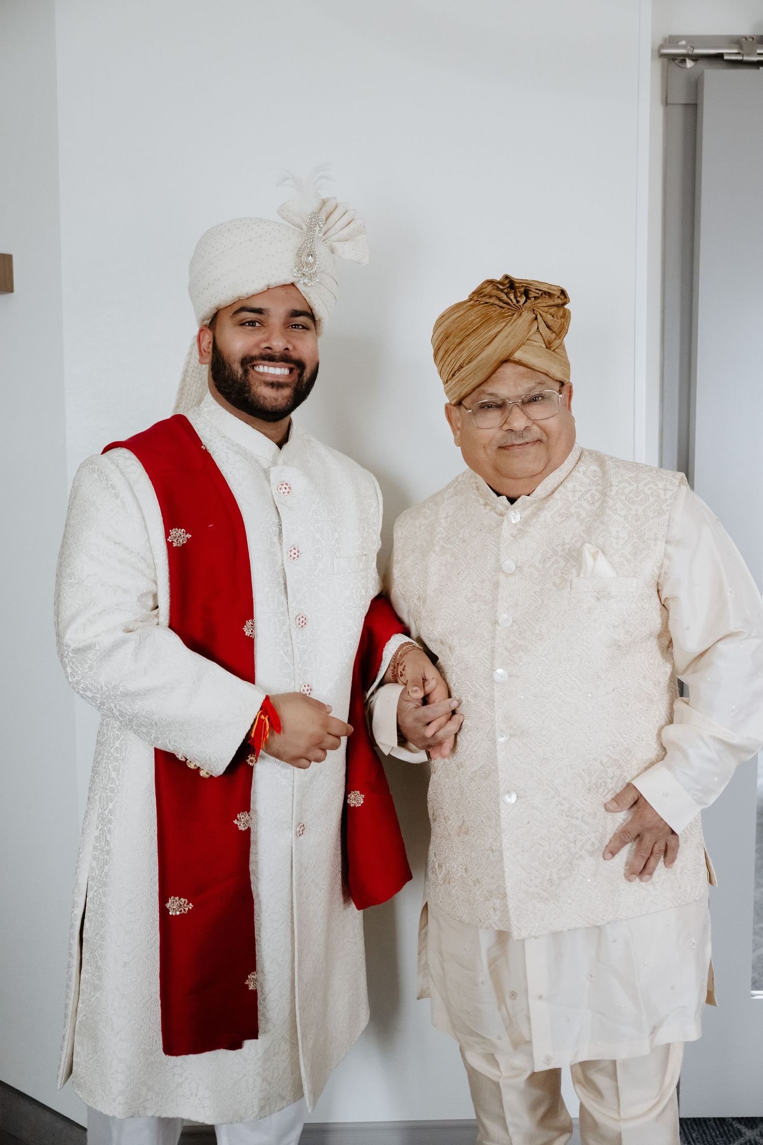 Two men in traditional Indian wedding attire, sherwani and turbans, posing together indoors.