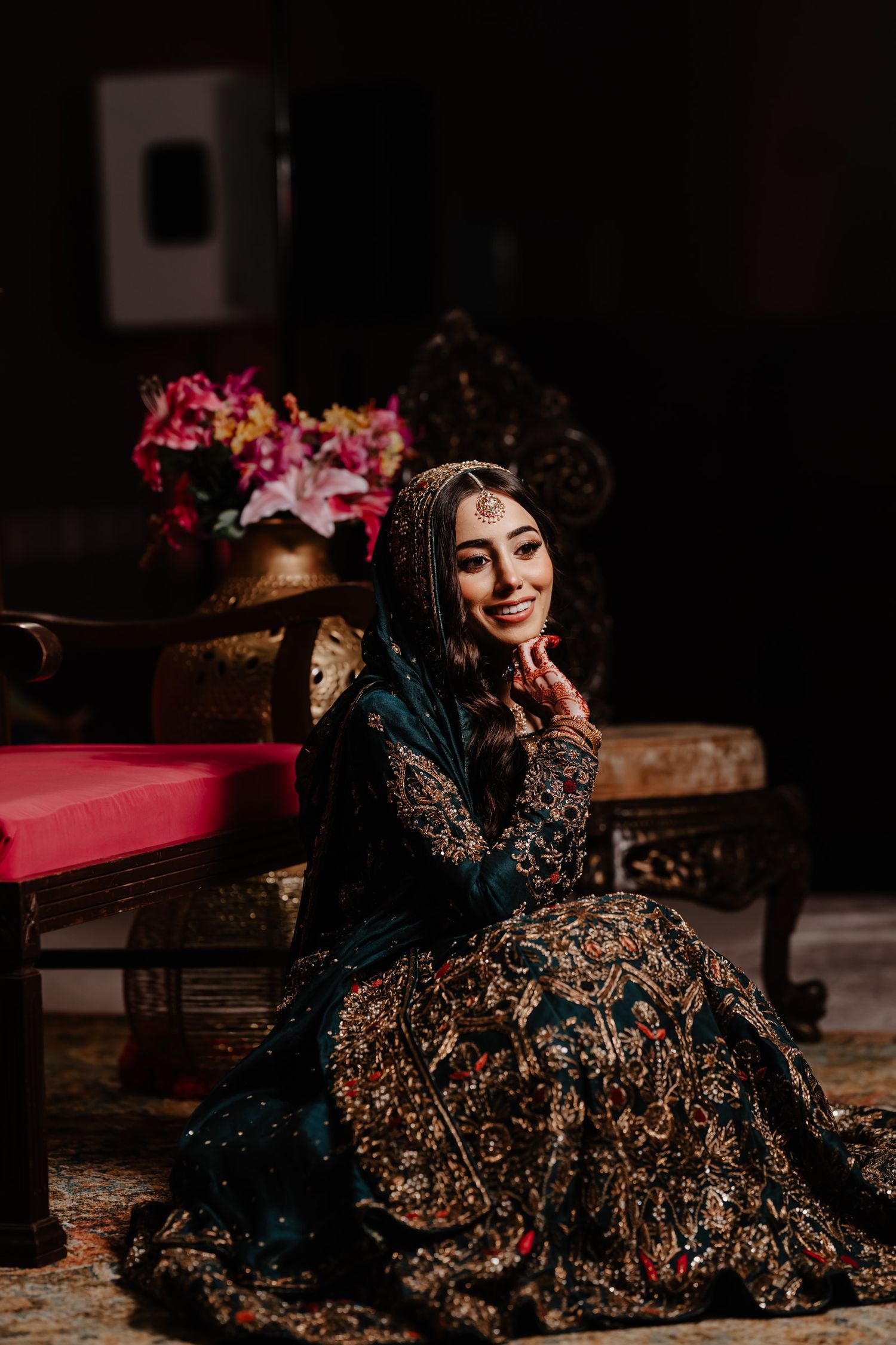 Traditional South Asian bridal attire featuring an intricately embroidered dark gown with gold details in a moody setting.