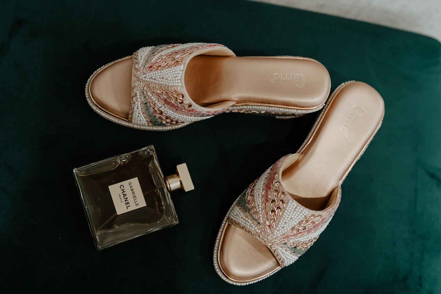 Elegant beige bridal shoes displayed on a dark teal surface with soft lighting.