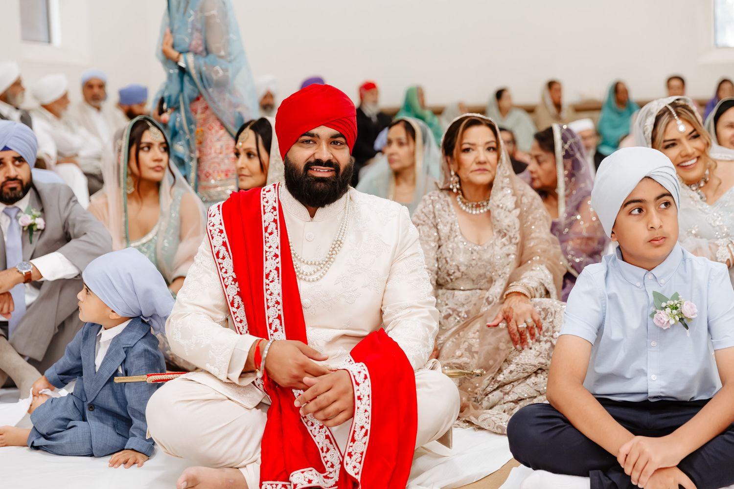 People gather at a Sikh temple ceremony wearing traditional attire with red and white garments in focus.