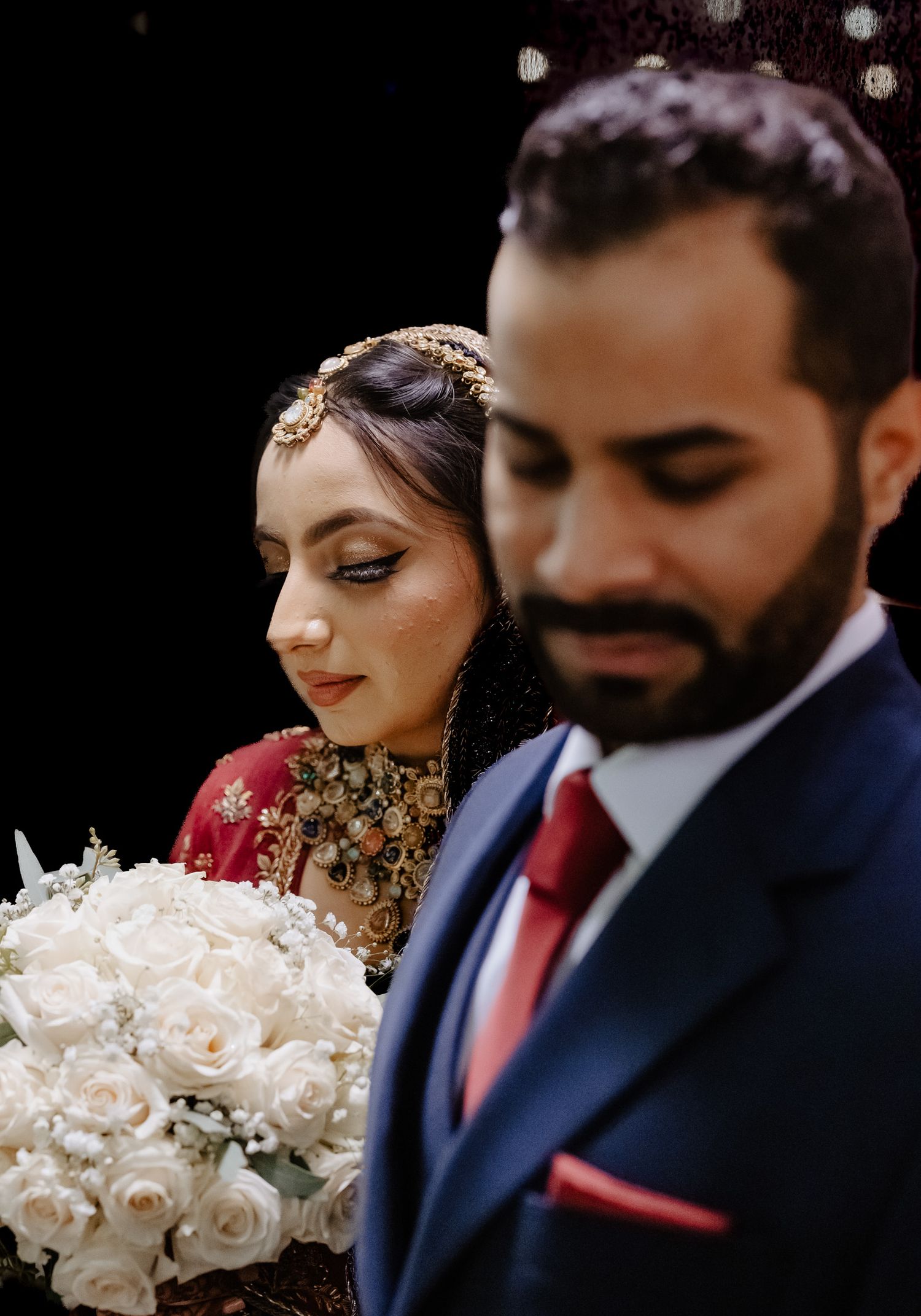 A romantic wedding couple poses with a white rose bouquet against a dark background.