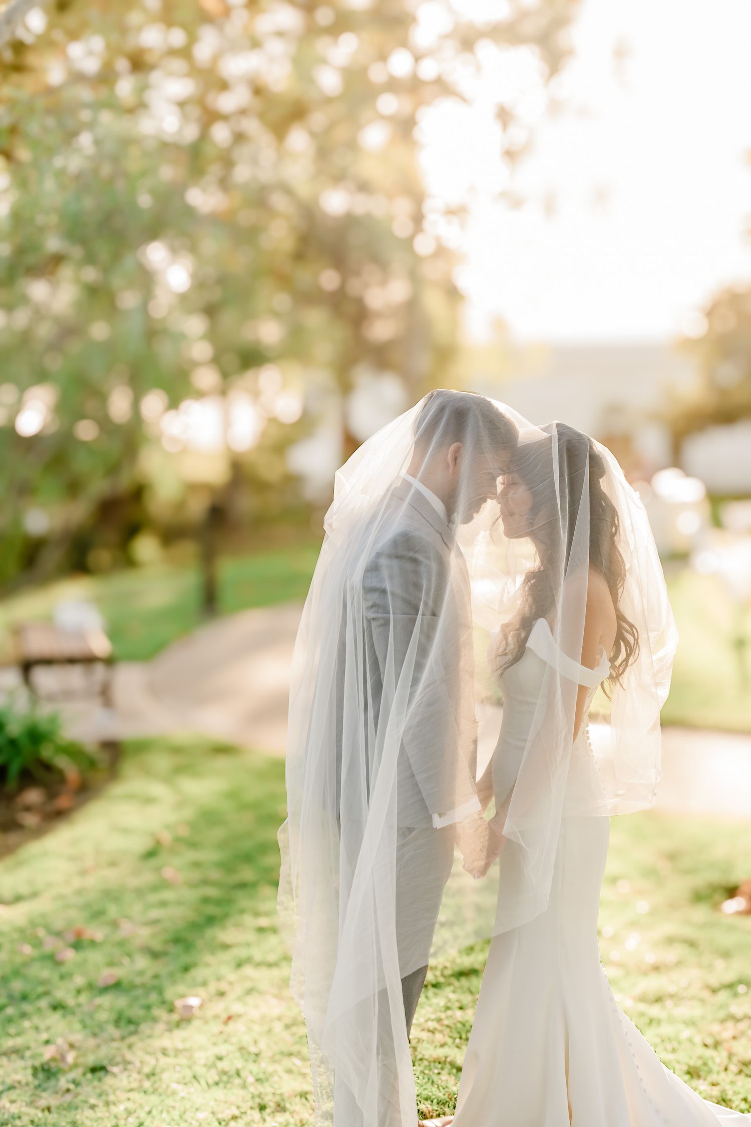 A romantic sunset wedding photoshoot shows a couple embracing under a flowing veil in a garden setting.