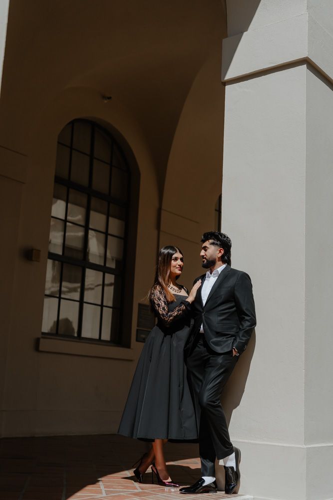 Elegant couple in black formal attire posing together against white architectural columns outdoors.