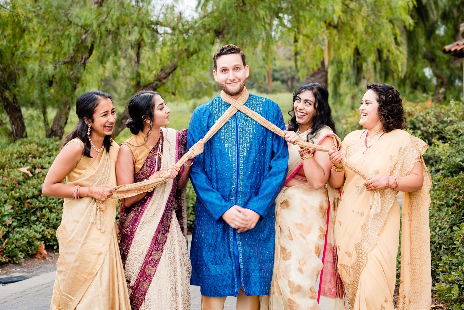 A group wearing traditional Indian attire in peach and blue colors poses together outdoors in a garden setting.