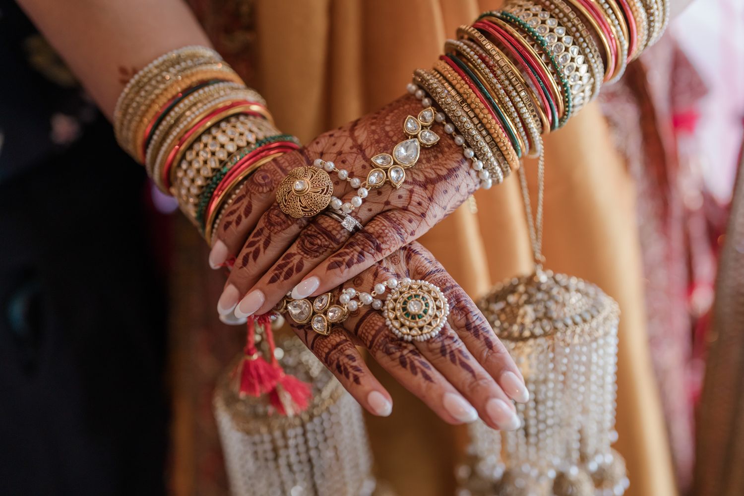 Traditional Indian bridal hands adorned with intricate henna designs and gold bangles during wedding ceremony.