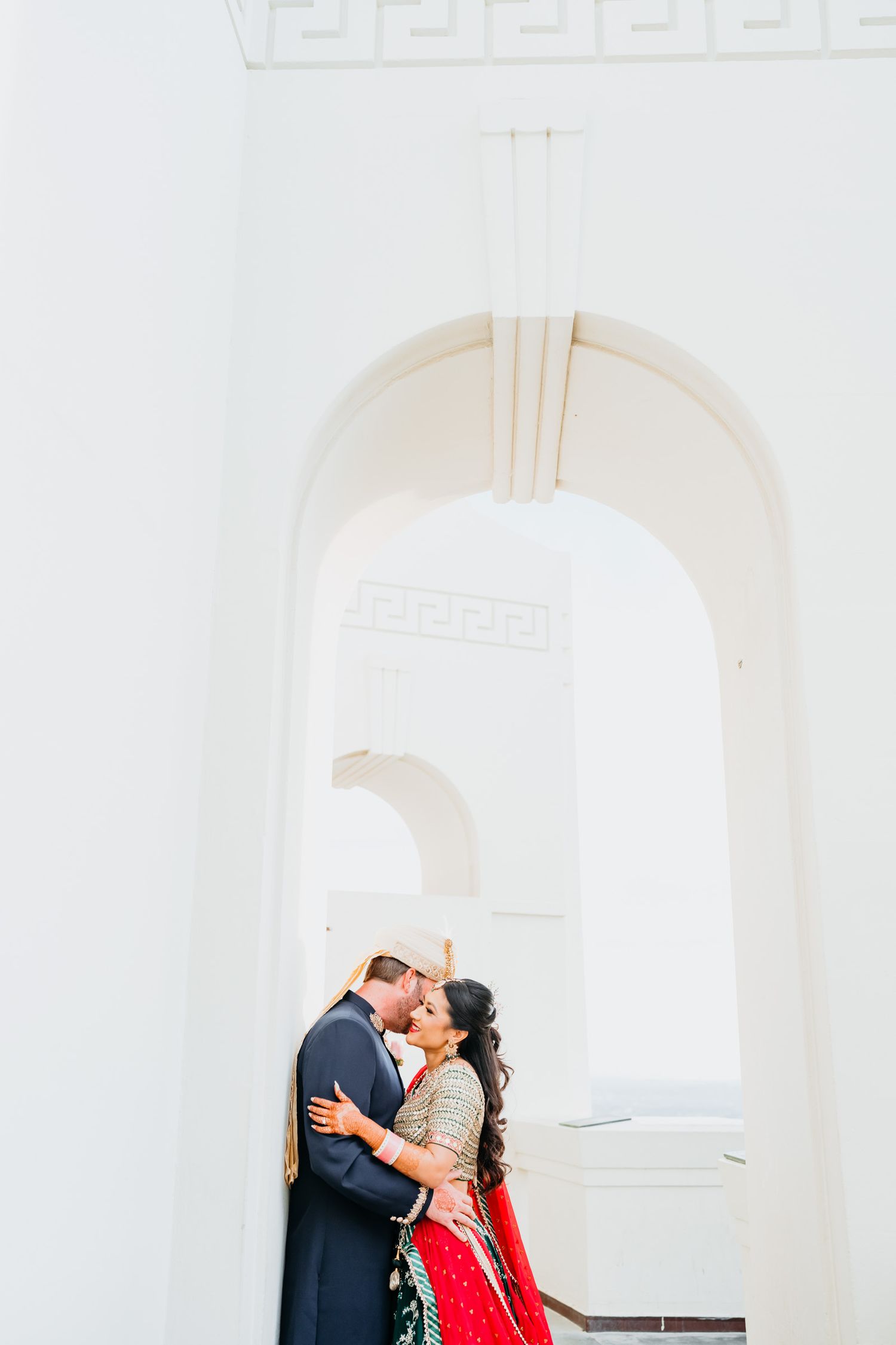 Couple embracing under elegant white archways in a romantic architectural setting.