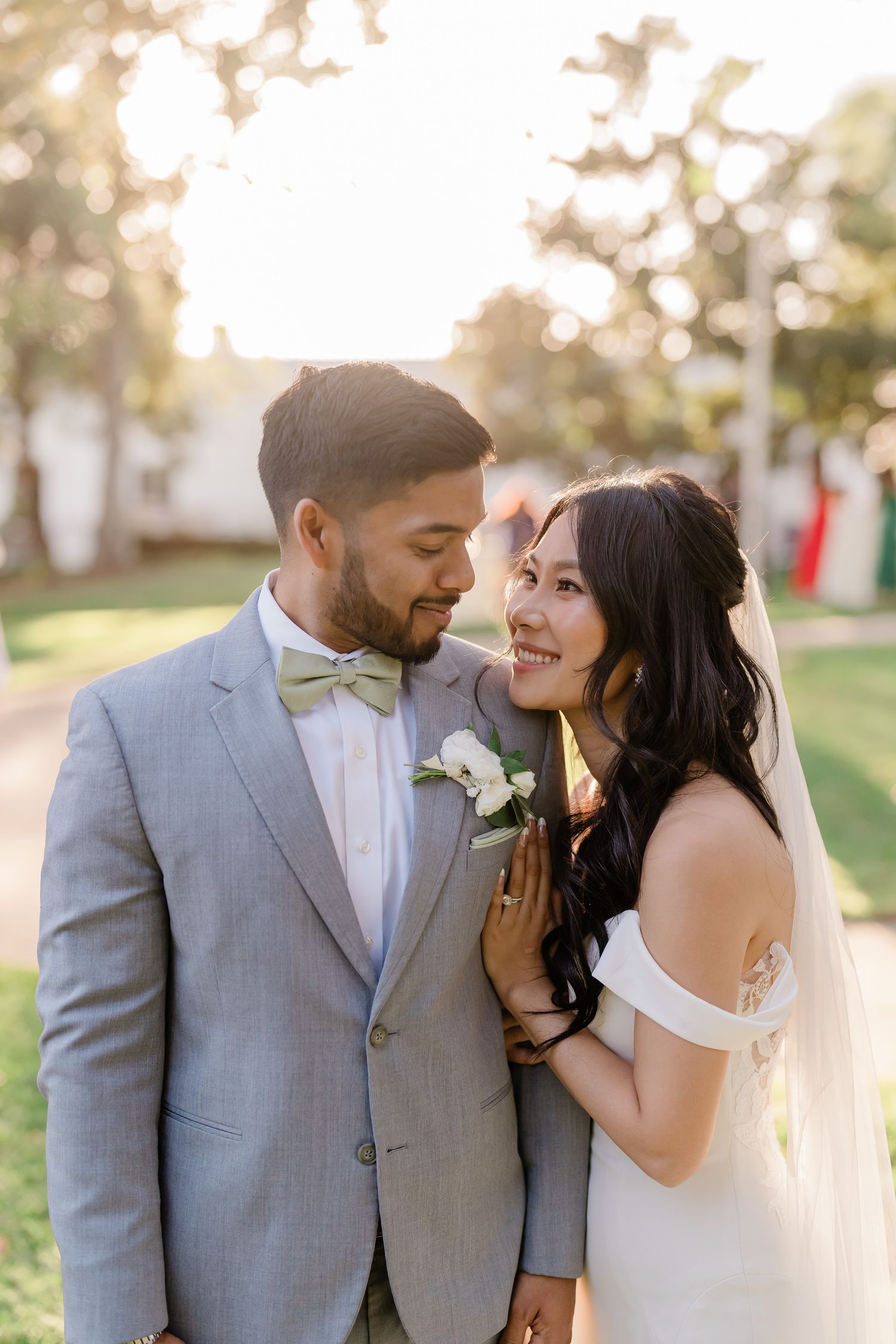 A romantic wedding portrait of a couple in formal attire embracing outdoors during golden hour sunset.