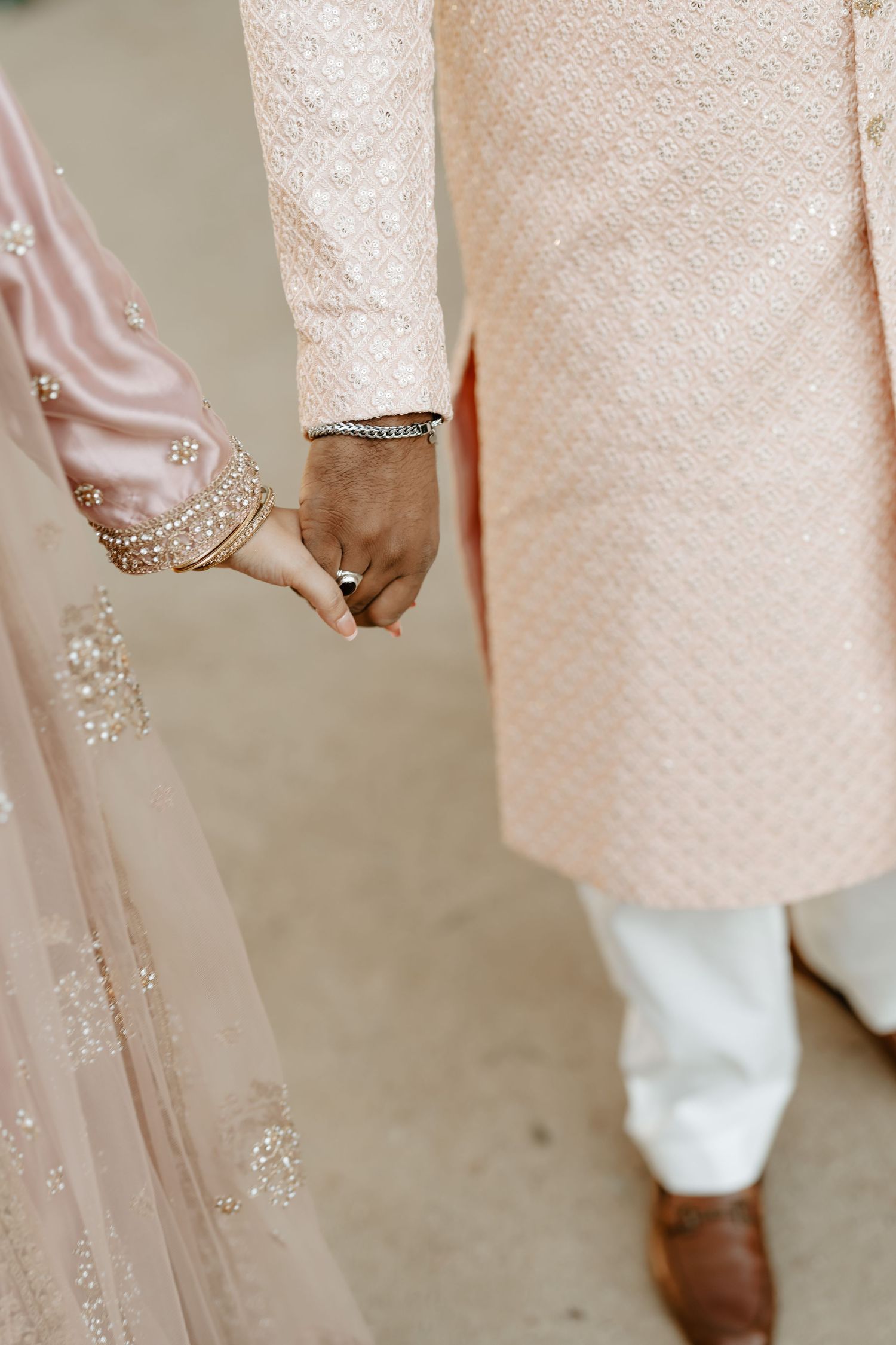 Close-up of hands holding while wearing elegant South Asian wedding attire with intricate embellishments.