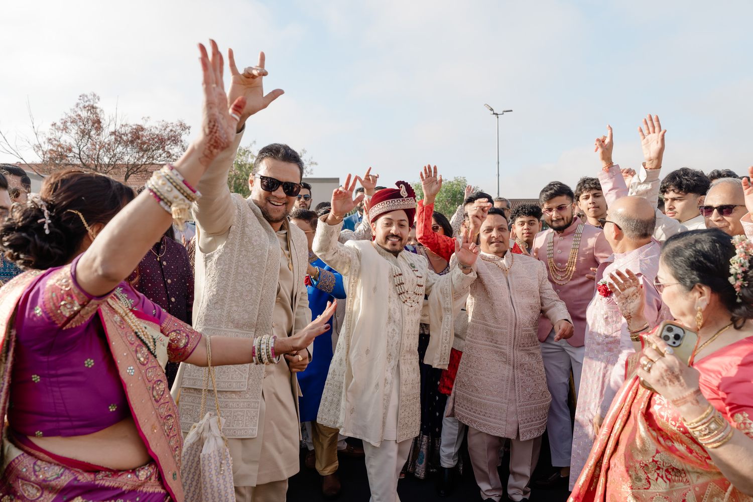 Wedding guests dance and celebrate with raised arms at an outdoor reception party.