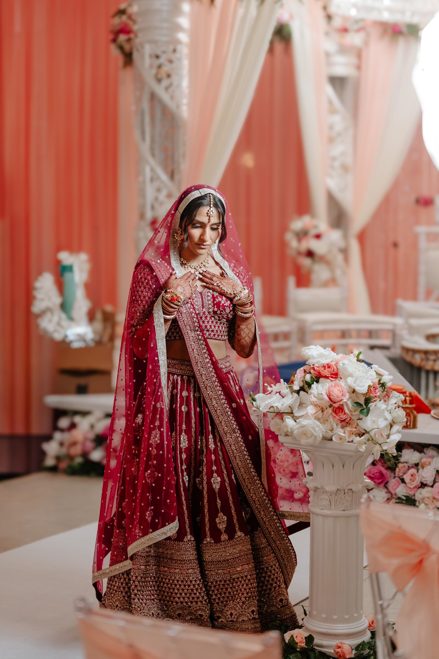 Traditional Indian wedding decor with red lehenga and floral arrangements in an elegant indoor venue.