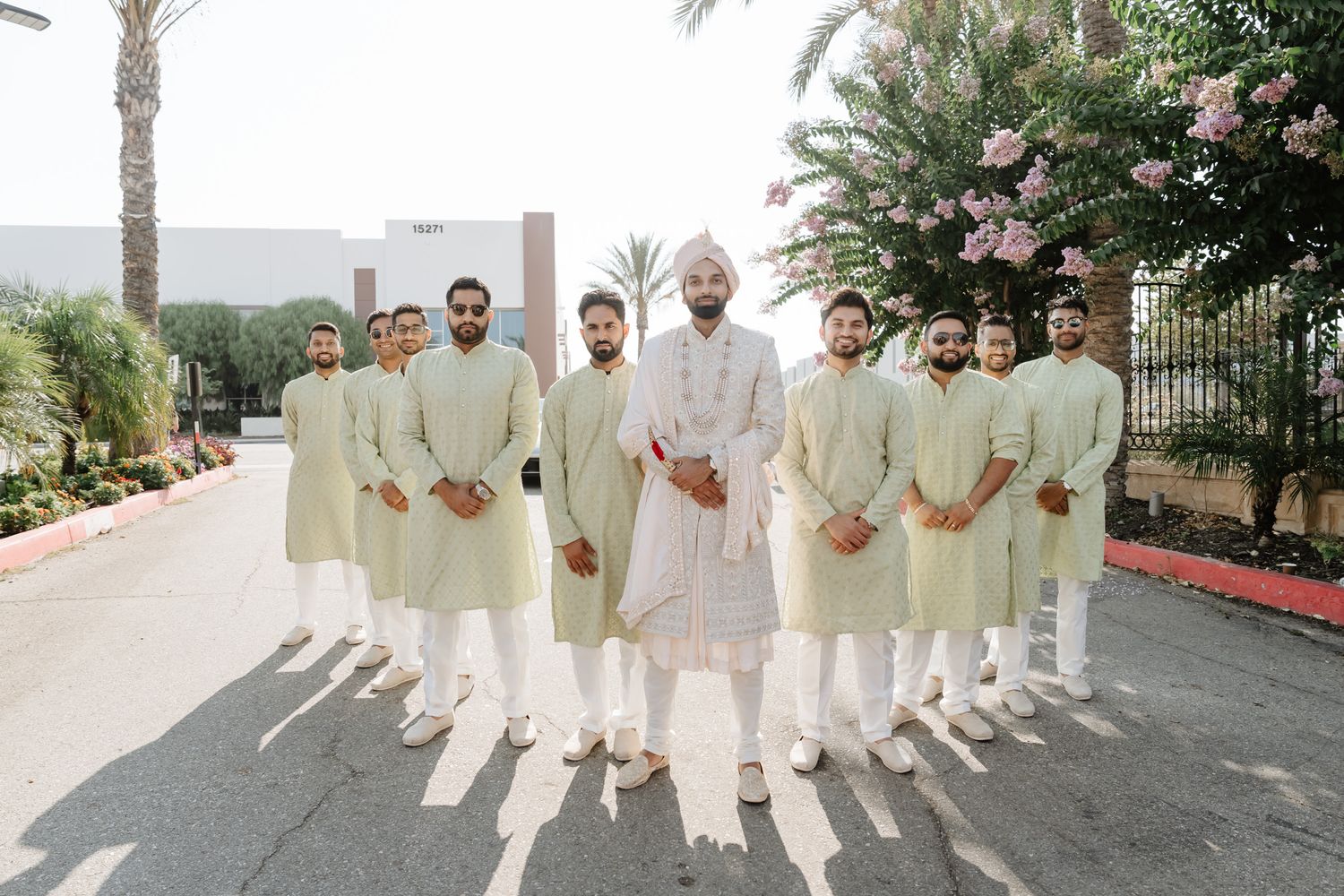 Groomsmen in matching cream colored traditional Indian wedding attire pose together outdoors.
