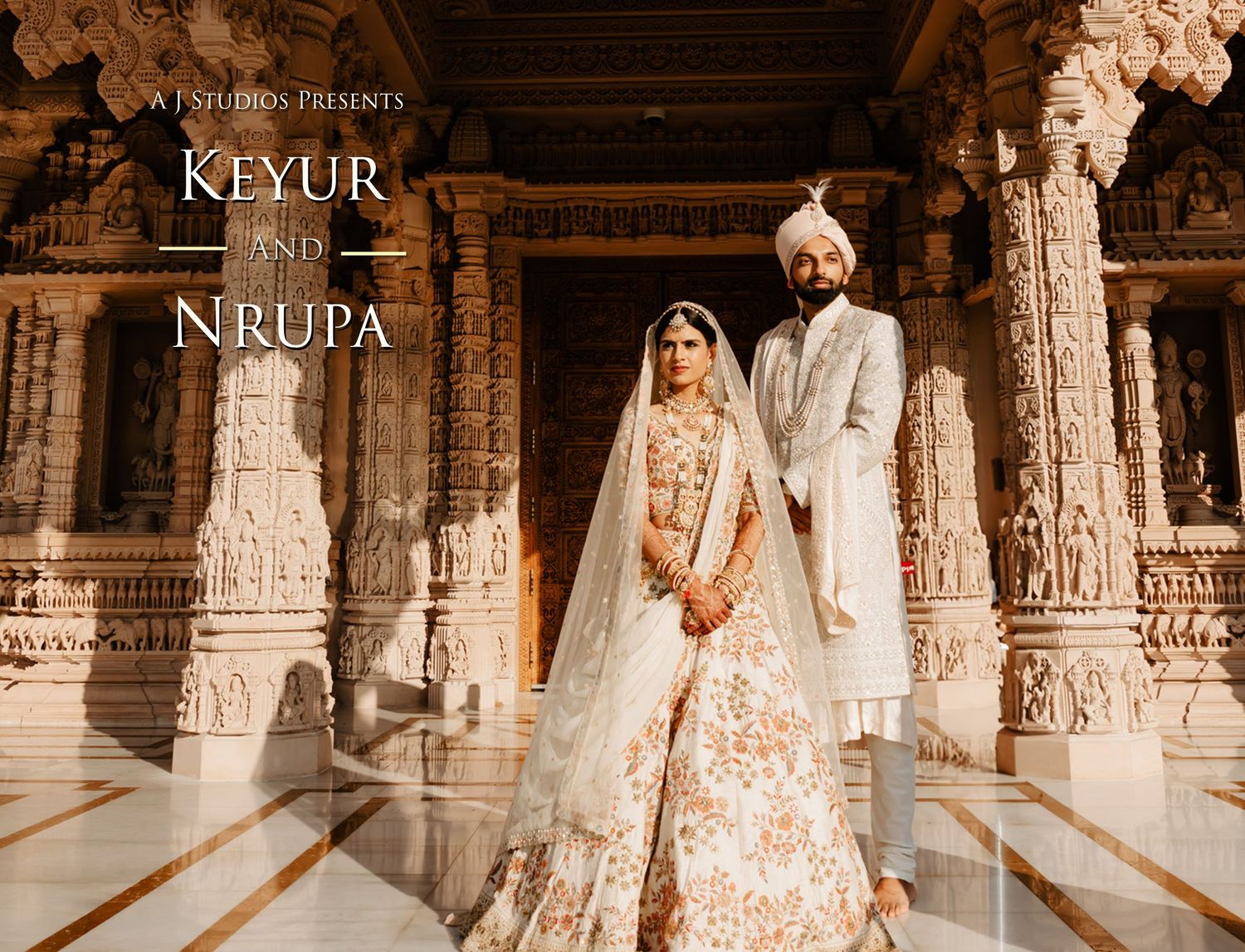 A couple in traditional Indian wedding attire poses in front of an ornately carved stone temple corridor.