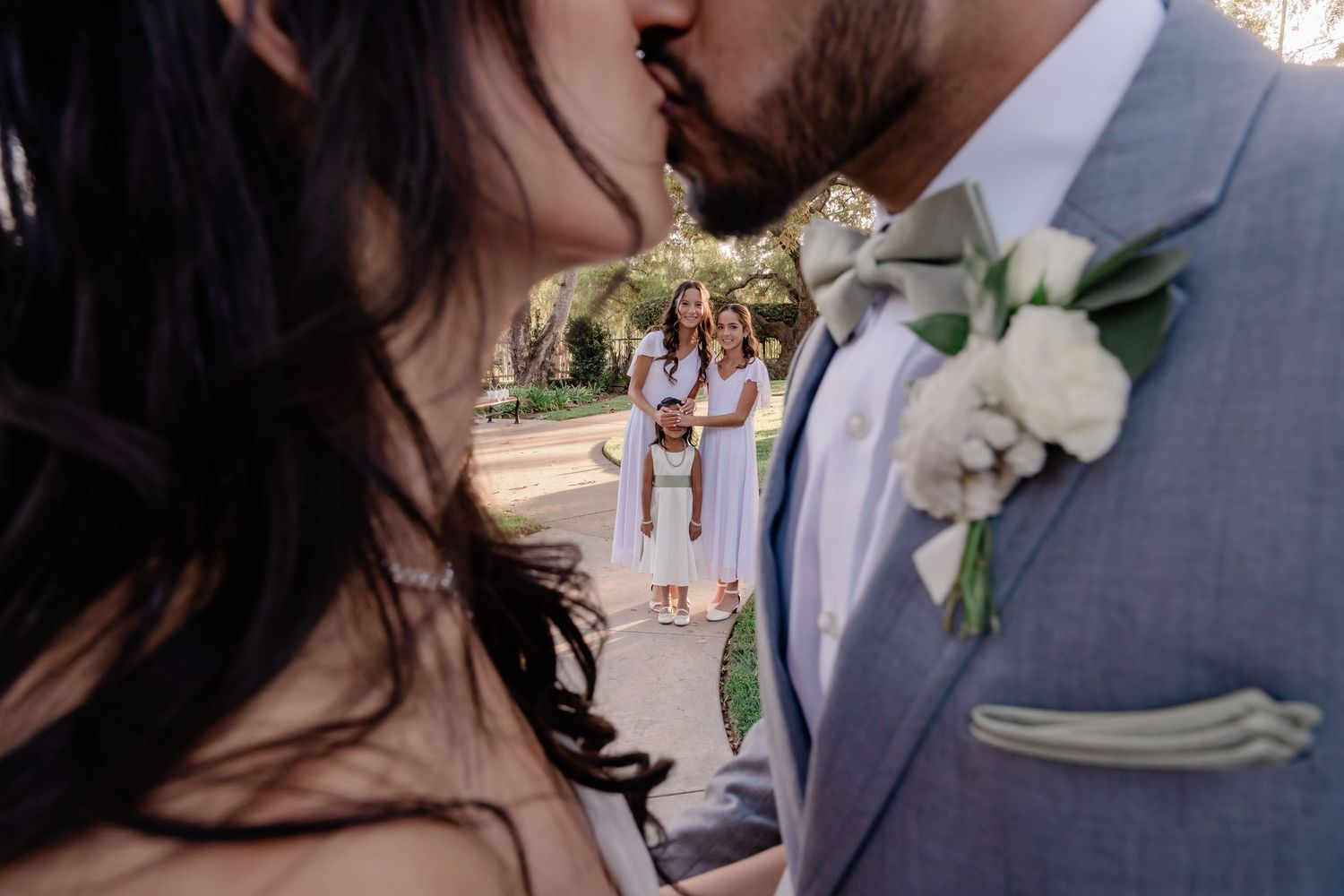Close-up shot of a romantic wedding moment with a light blue suit and white boutonniere against a garden backdrop.
