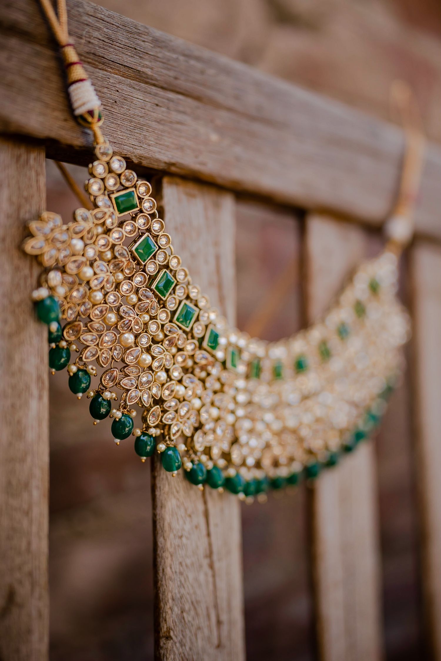 Ornate gold and emerald Indian bridal jewelry with intricate kundan work displayed against wooden background.
