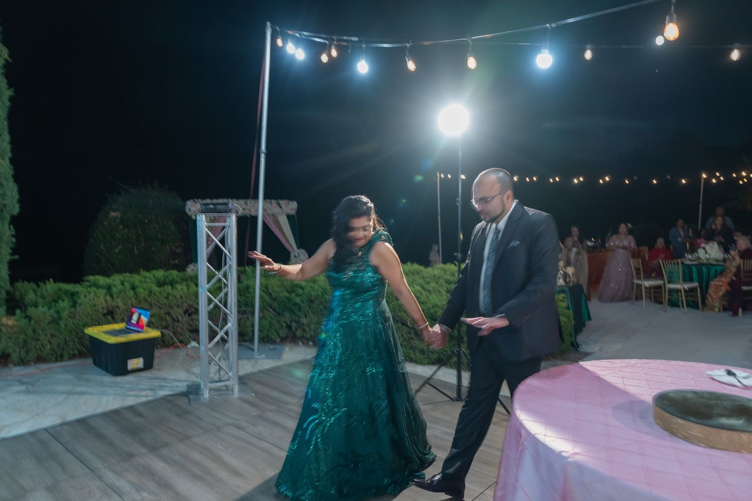 Outdoor evening wedding reception with illuminated dance floor and string lighting.