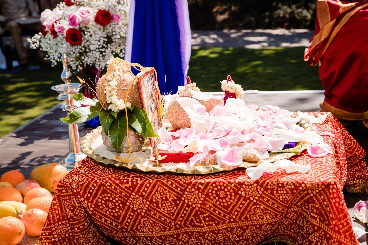 Pink and burgundy floral arrangements with rose petals decorate an ornate table setting with rich textured tablecloths.