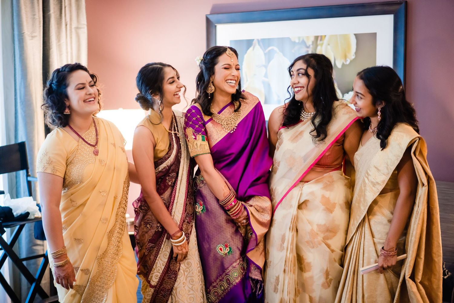 A group of people wearing traditional Indian saris and formal attire laugh together at a festive celebration.
