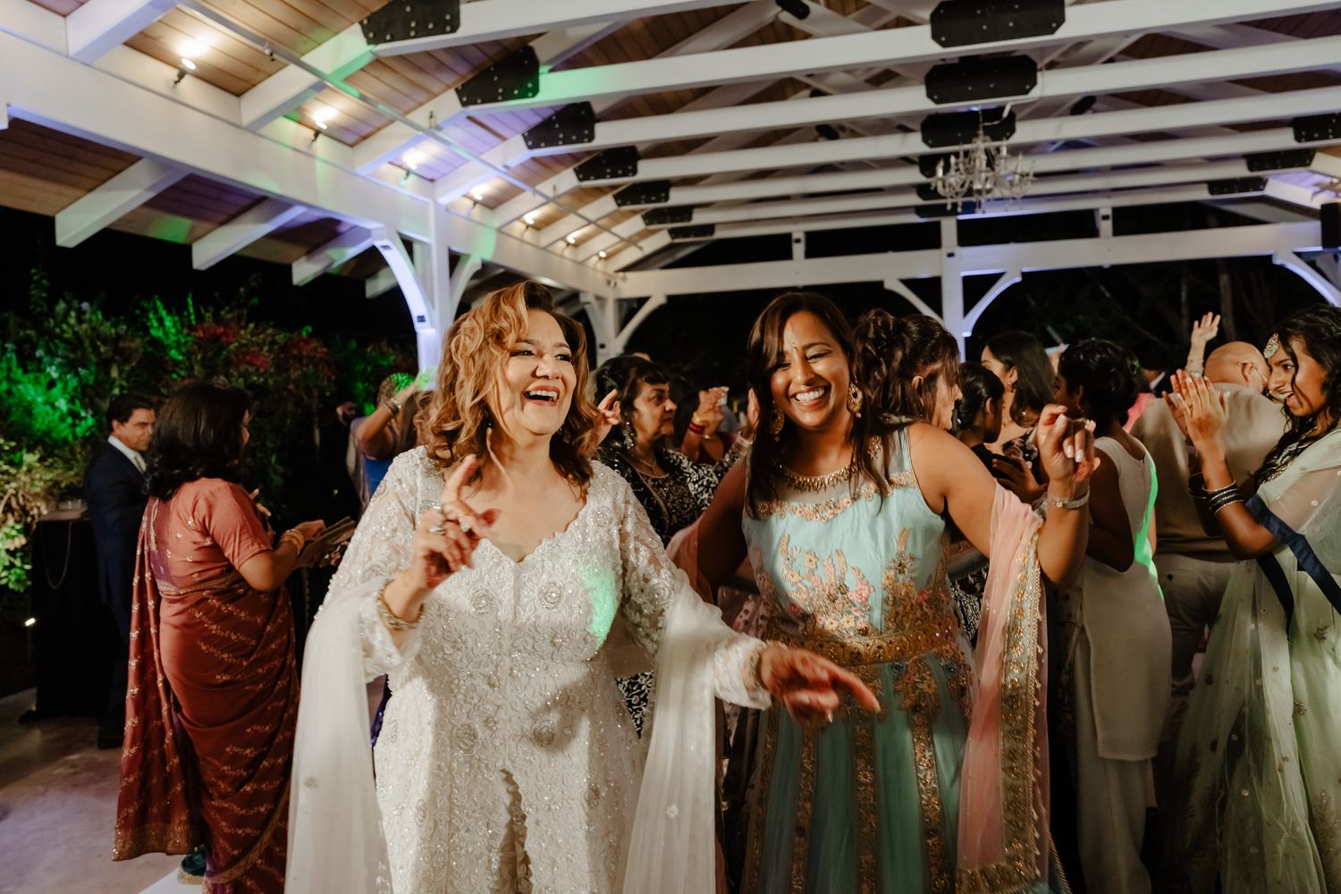 Wedding celebration with guests dancing under rustic wooden beams and string lights.