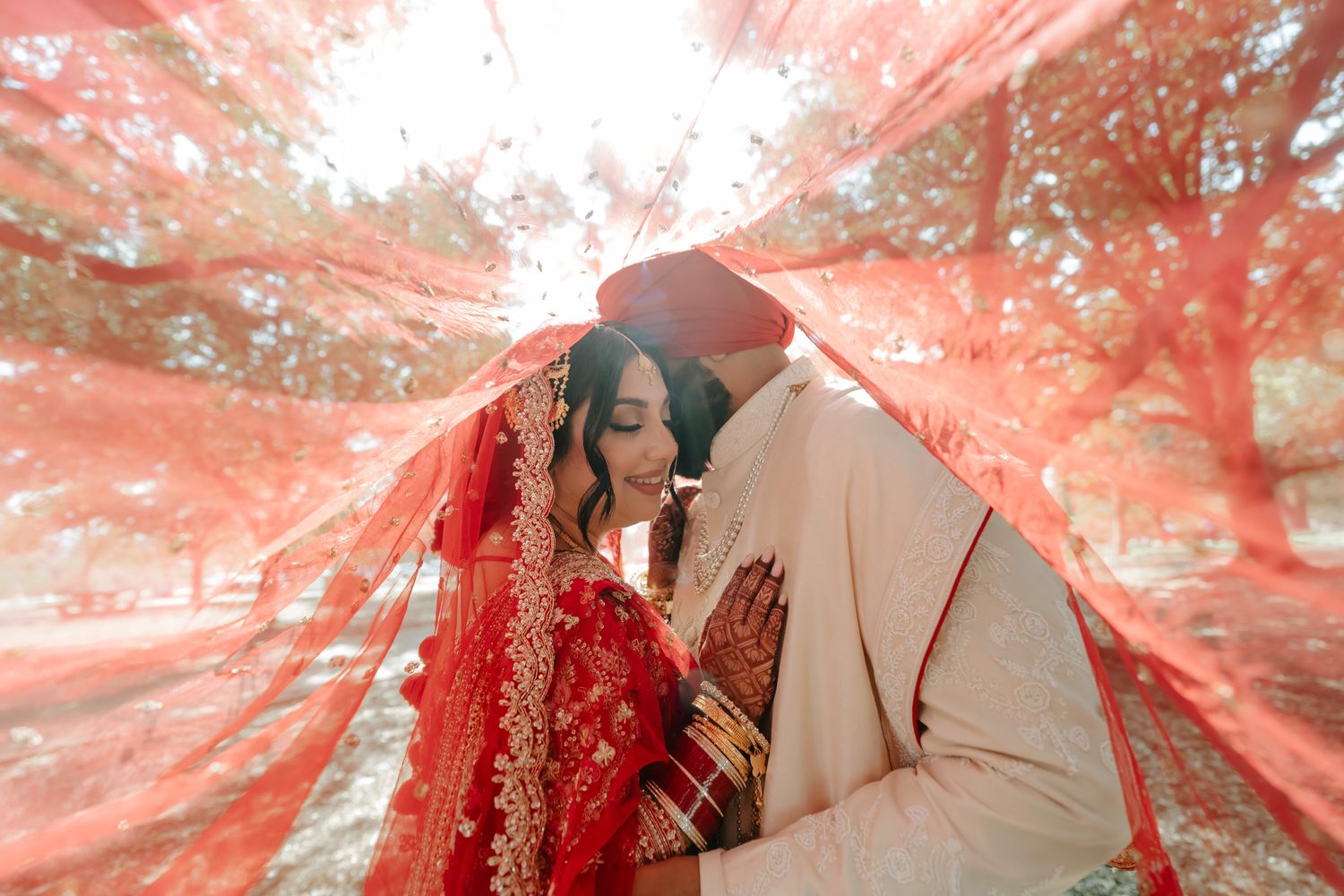 Wedding couple under flowing red dupatta creating romantic atmosphere.