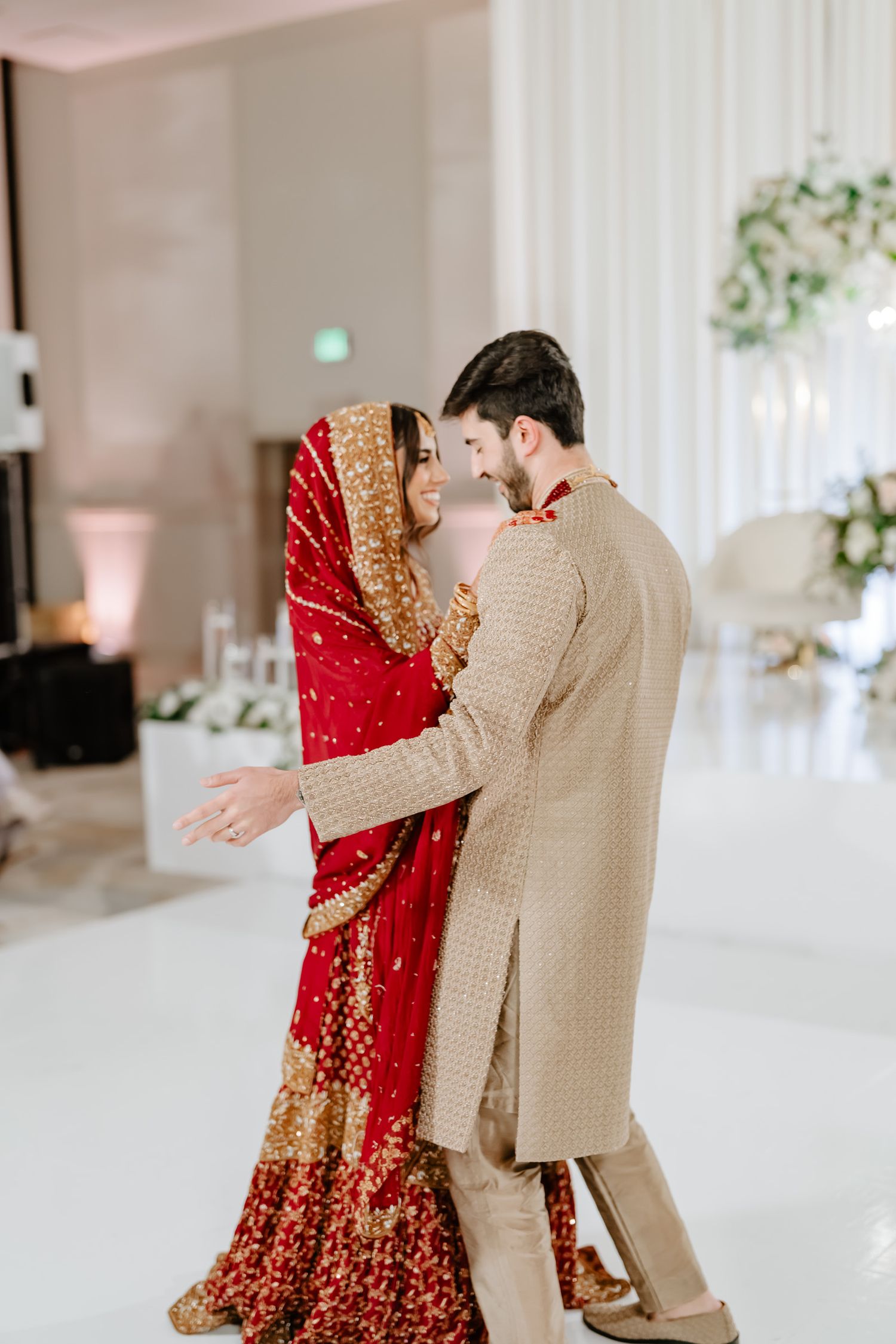 A couple shares an intimate moment during their wedding celebration, with the bride wearing a traditional red and gold lehenga.