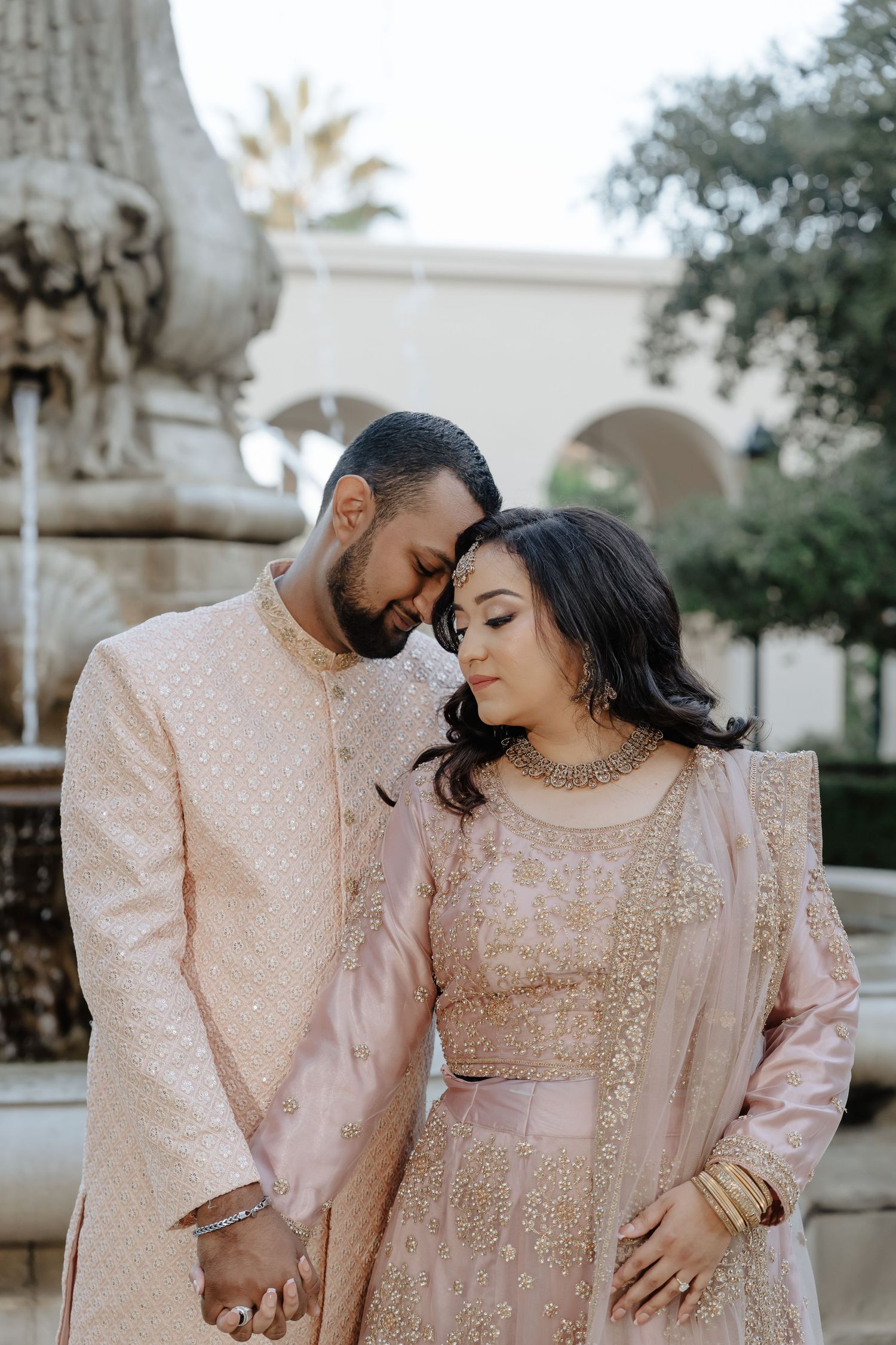 A romantic couple in matching blush pink traditional South Asian attire pose intimately together during a photo session.