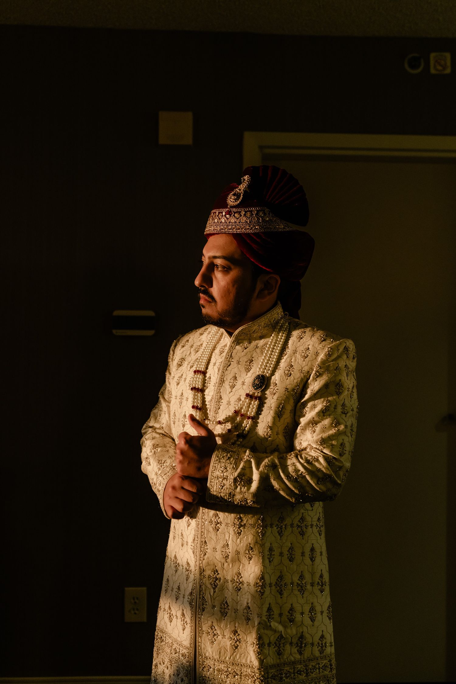 A performer in an ornate white costume and crown stands in dramatic lighting on a dark stage.
