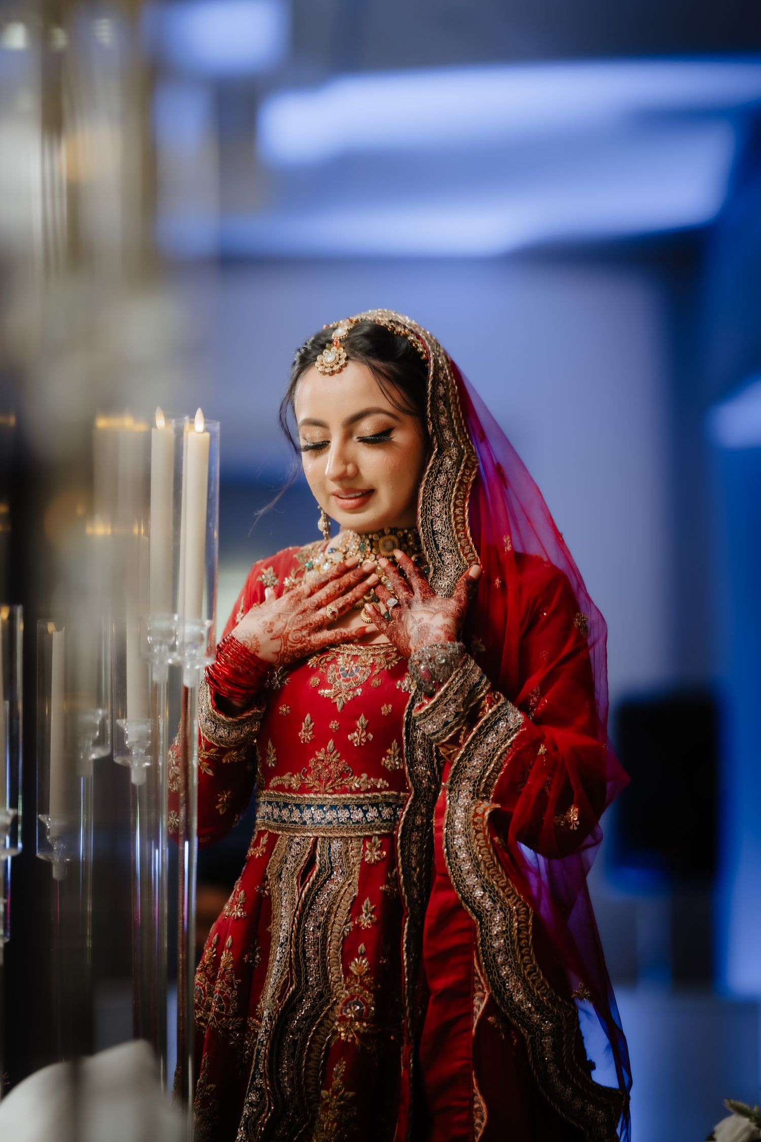 Traditional Indian bride in red lehenga with ornate gold embroidery and jewelry poses with graceful hand gestures.