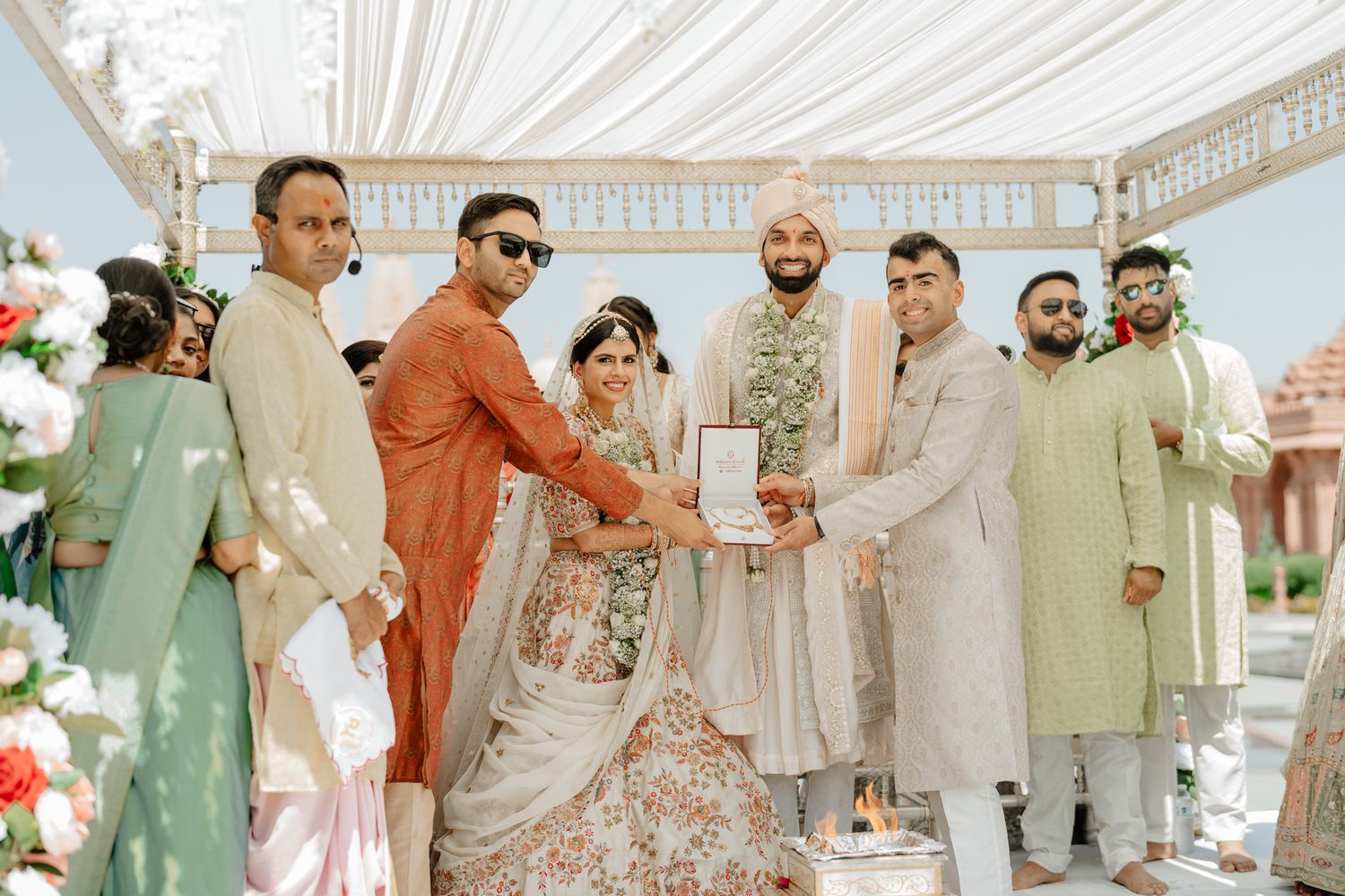 Wedding guests and family members gather under a white mandap for a traditional Indian ceremony celebration.