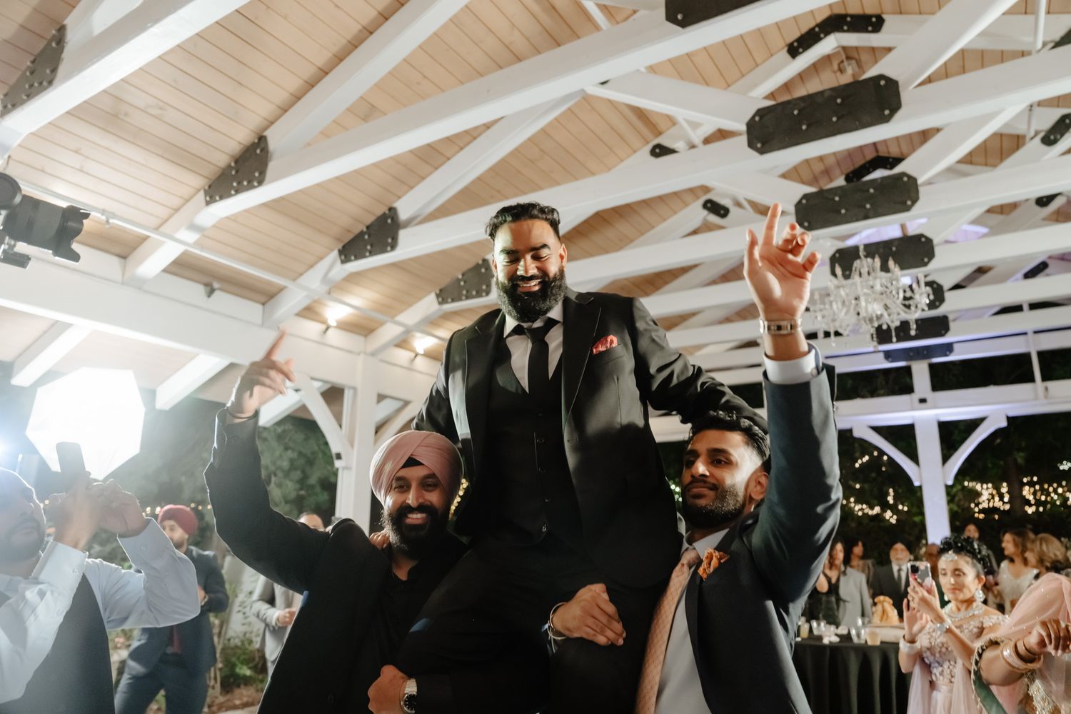 Wedding reception venue with exposed wooden beams and festive lighting overhead.