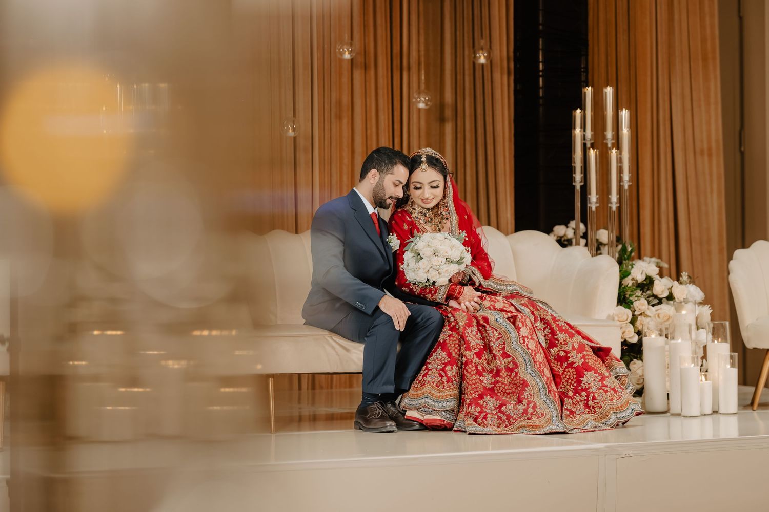 A couple in traditional wedding attire sits on the floor surrounded by elegant candles and decor.