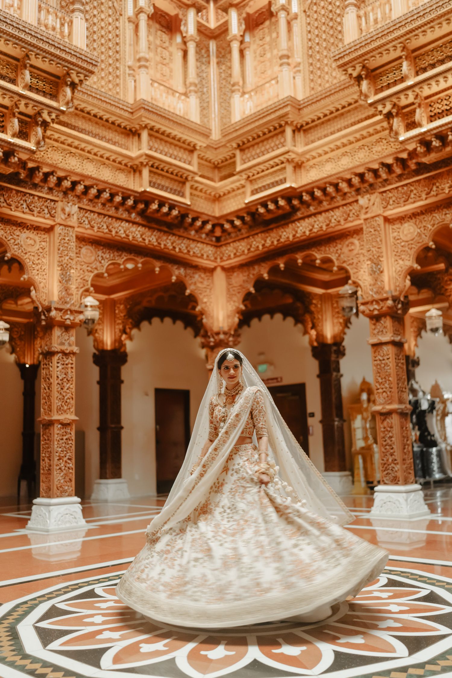 Ornate Indian palace interior with intricate carved pillars and geometric floor patterns featuring a flowing bridal gown.