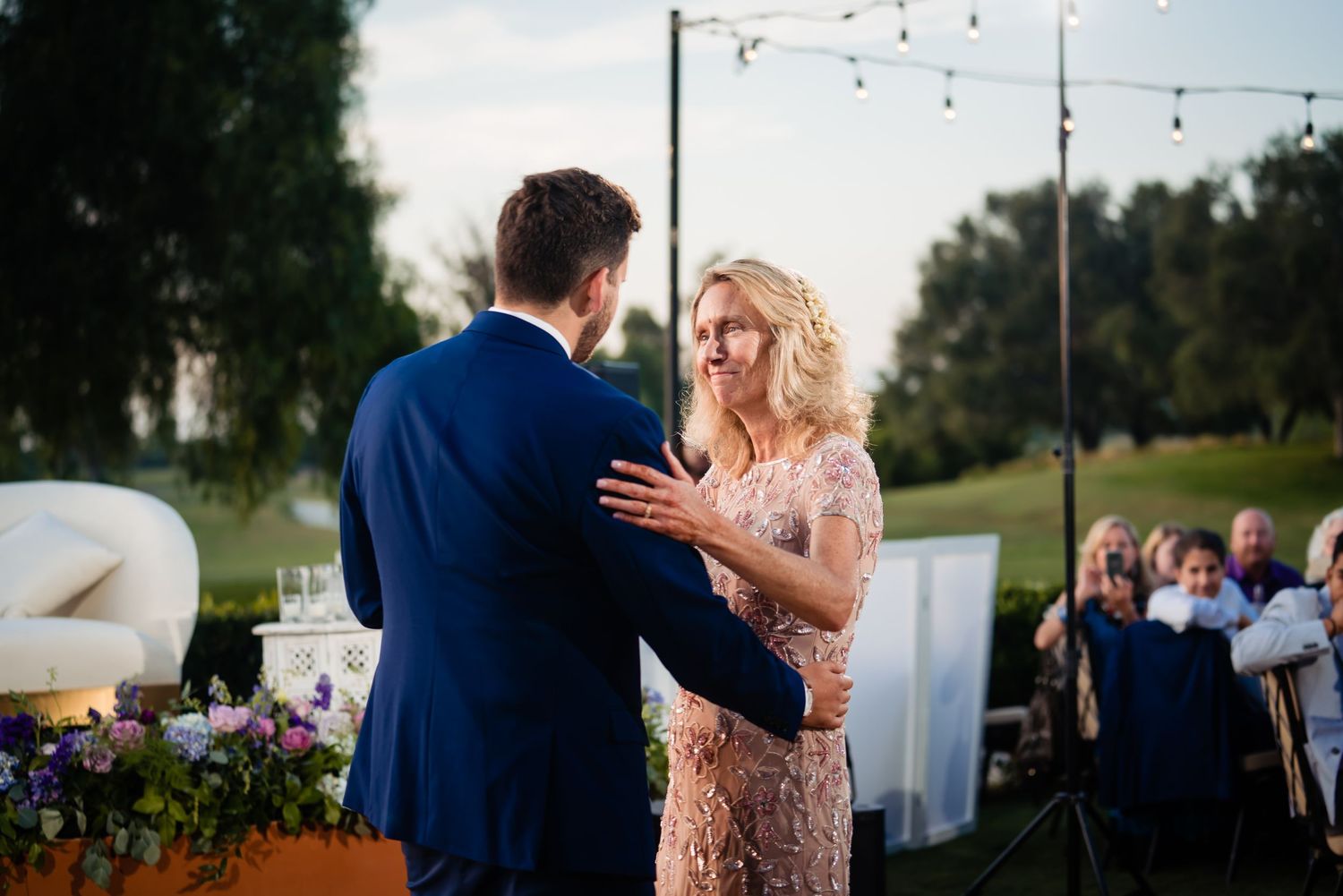 Outdoor wedding reception at sunset with string lights and white linens decorating the venue.