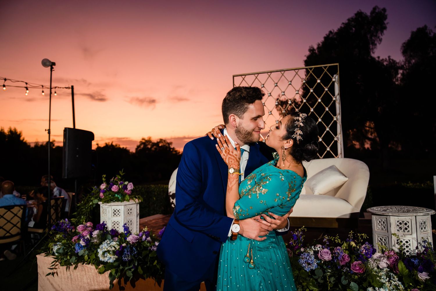 Silhouettes of a couple embracing against a vibrant orange sunset sky with power lines and trees in the background.