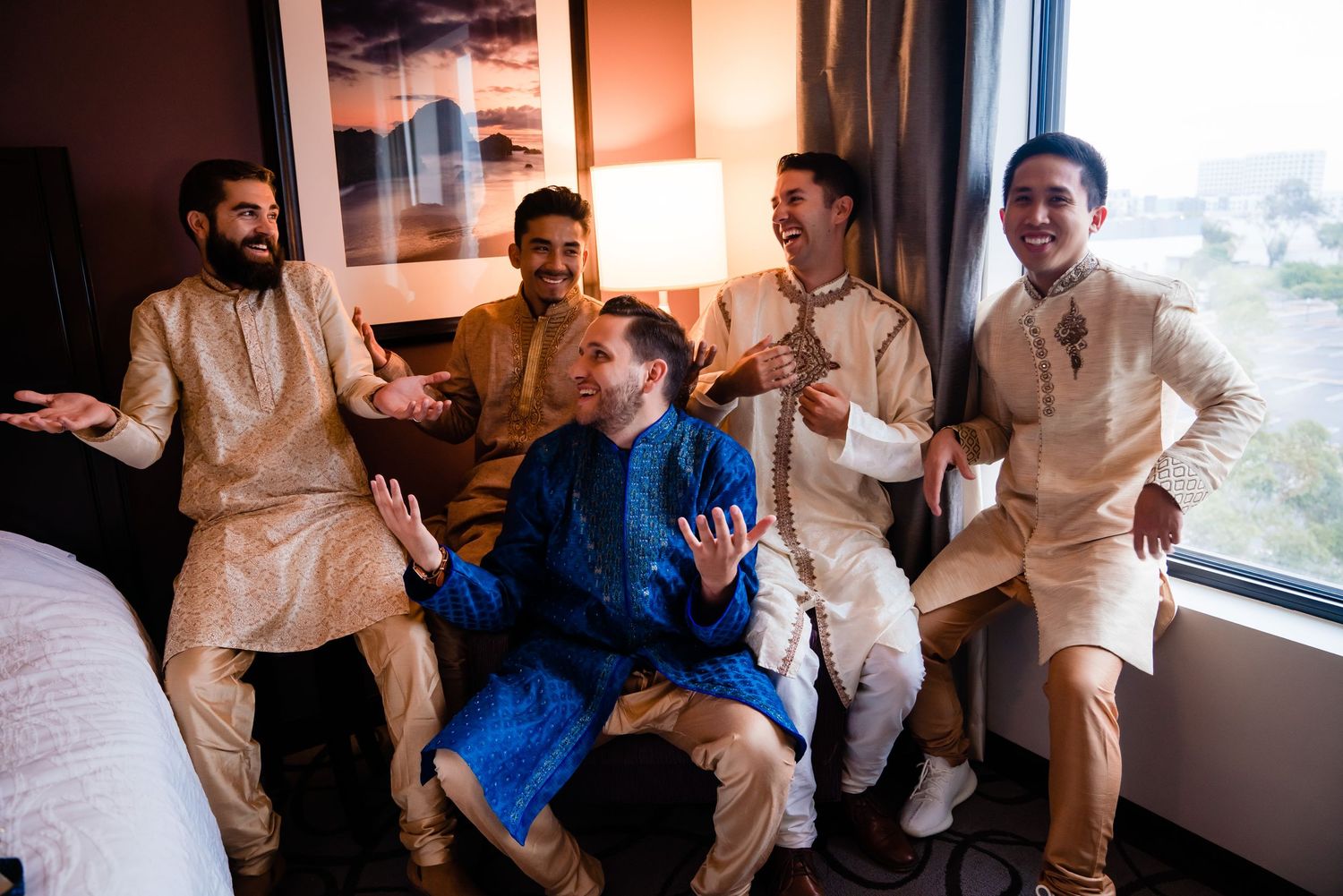 A group of people in traditional South Asian attire share a lighthearted moment together in a bright room.