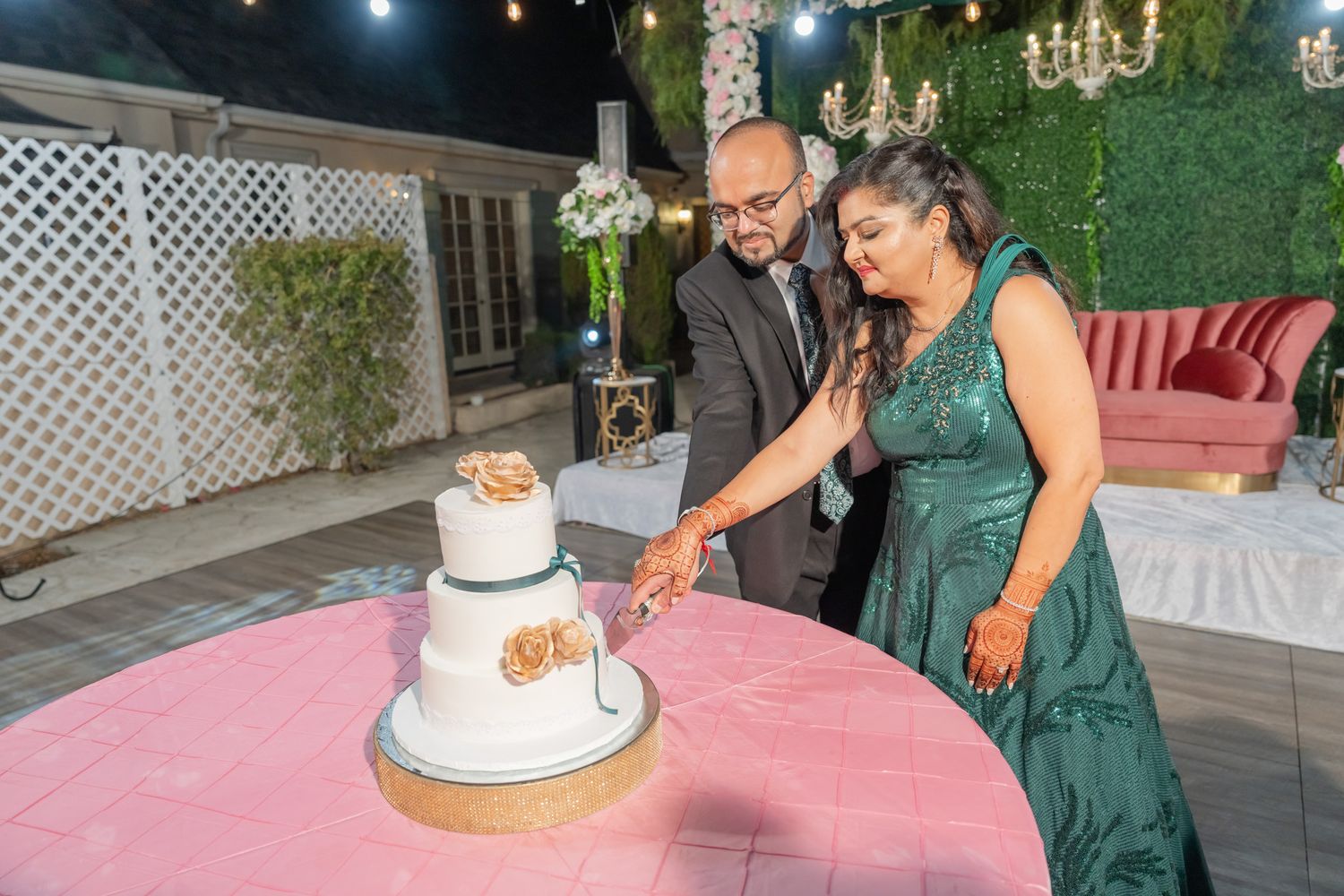 Wedding couple cutting their white tiered cake together at an outdoor evening reception.