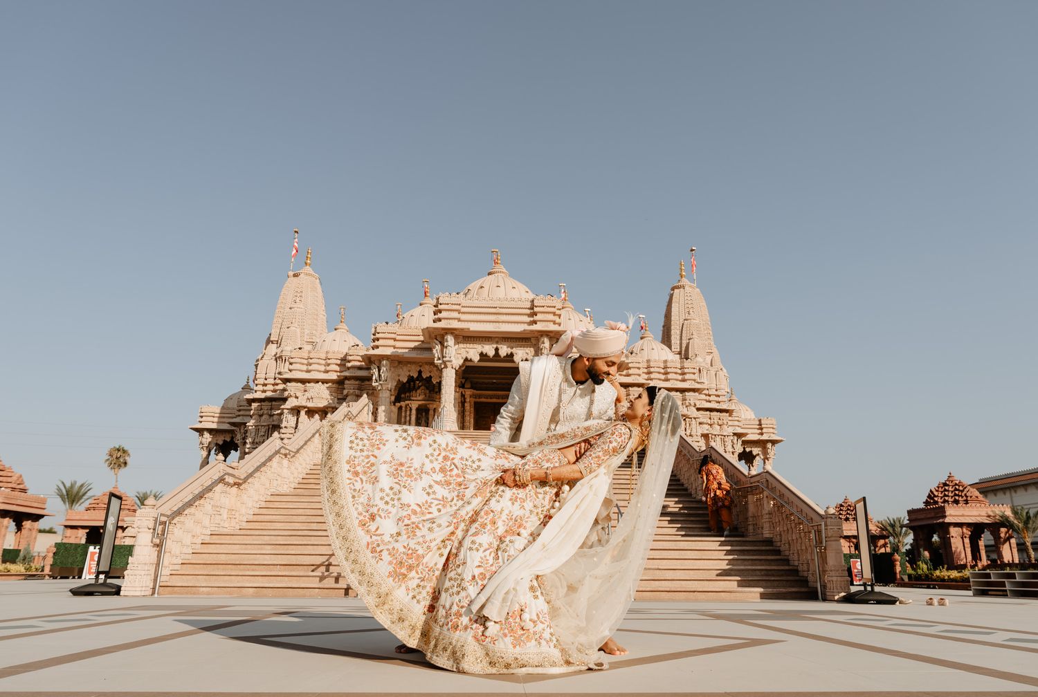 Panoramic view of ornate Indian temple architecture with beige stone spires and domes against clear blue sky.