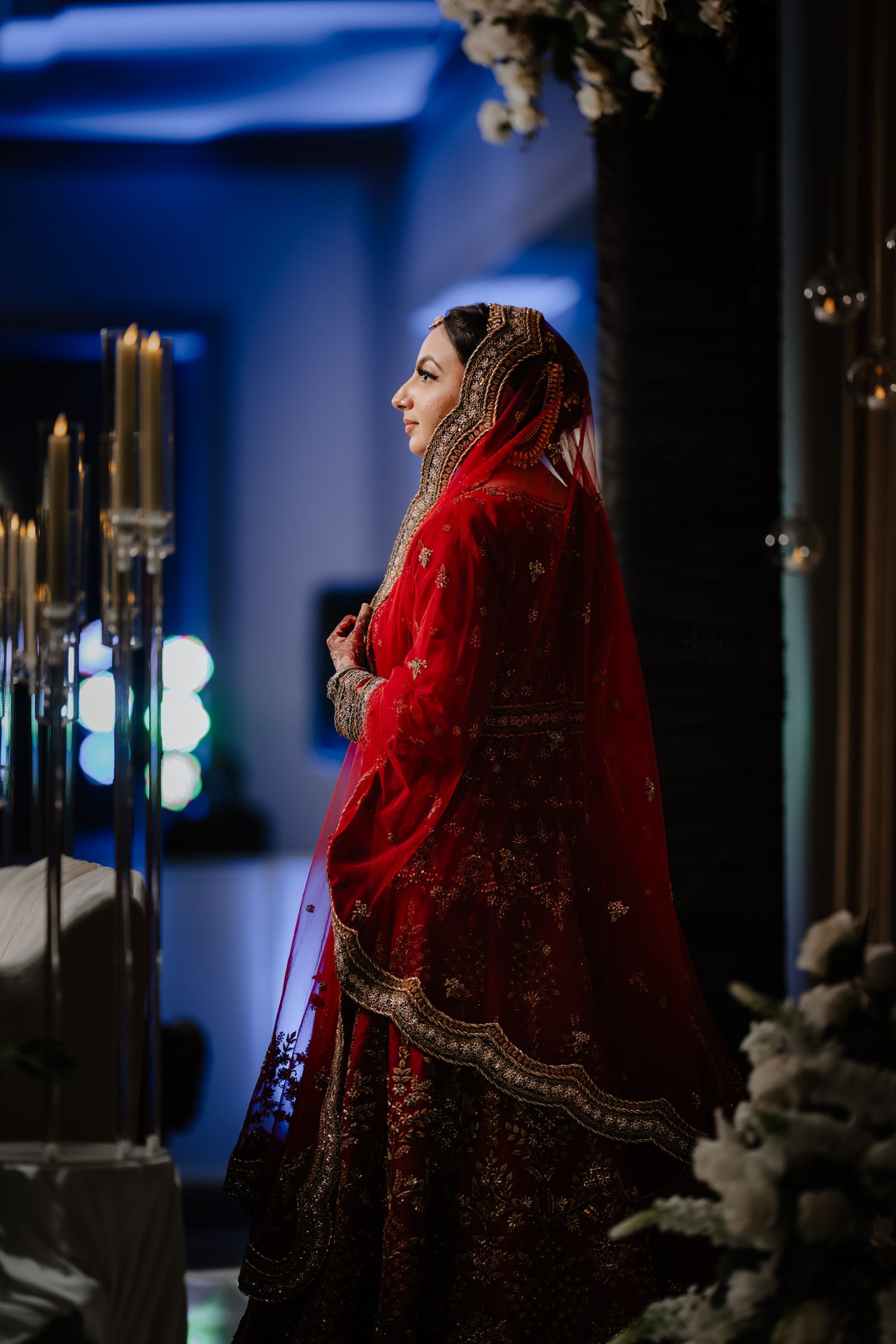 Dramatic bridal portraits featuring a red and gold lehenga against a deep blue background with moody lighting.