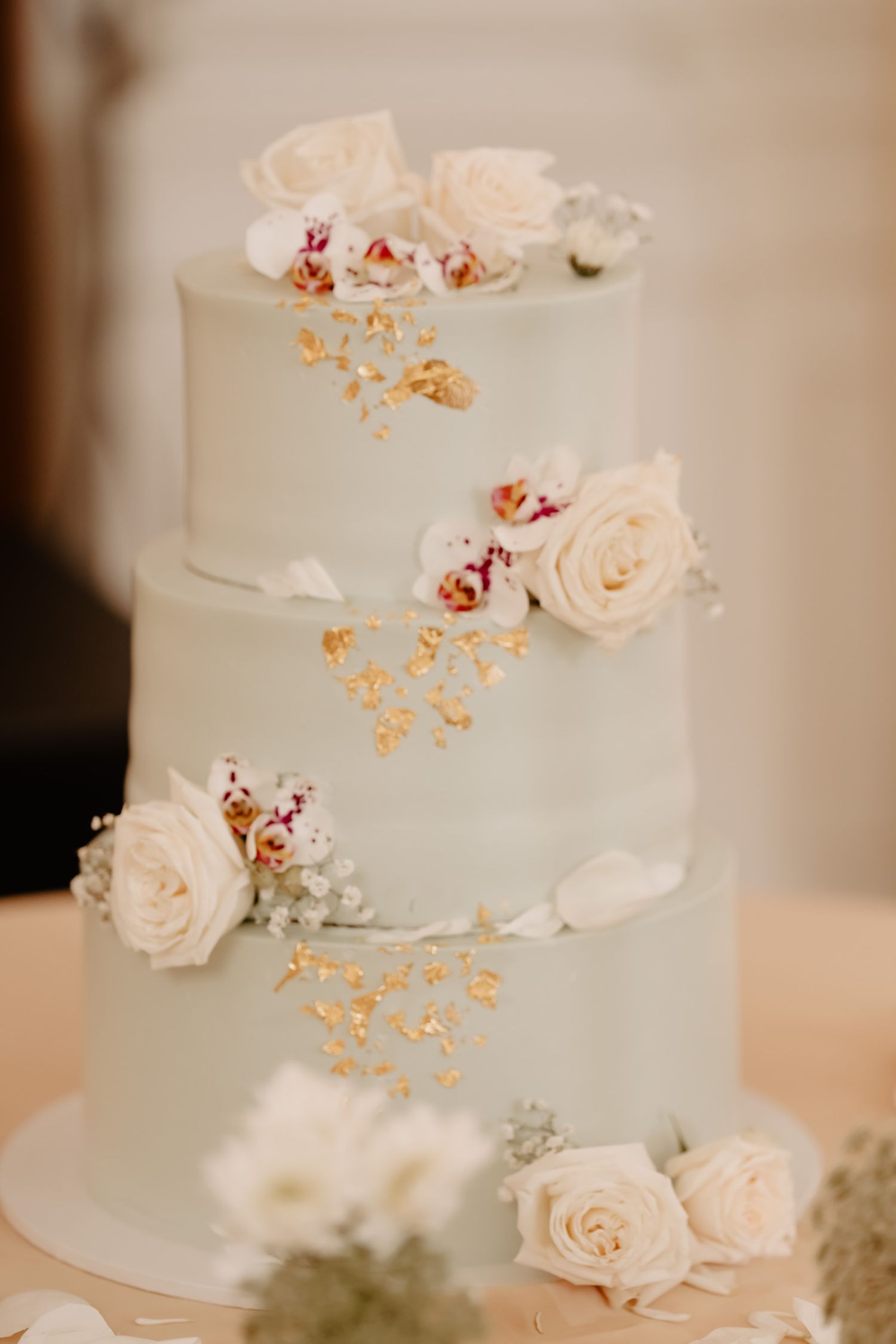 Elegant white wedding cake decorated with delicate pale roses and gold accents on display.