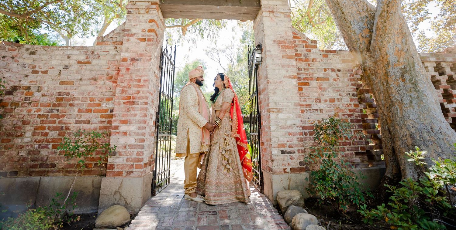 A couple shares an intimate moment under a rustic brick archway surrounded by greenery and natural light.