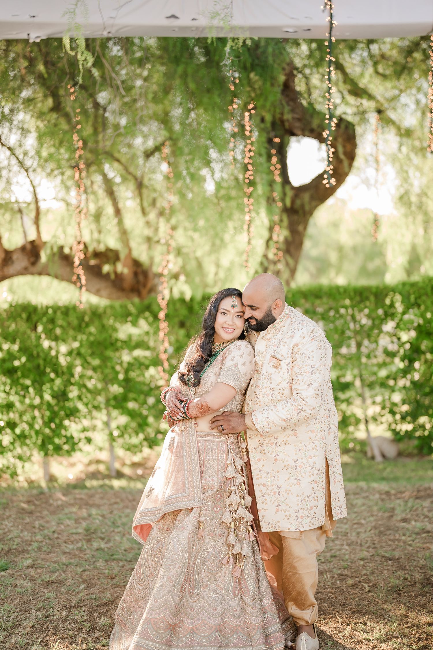A couple in coordinated beige outfits share tender moments together in a sunlit garden setting.