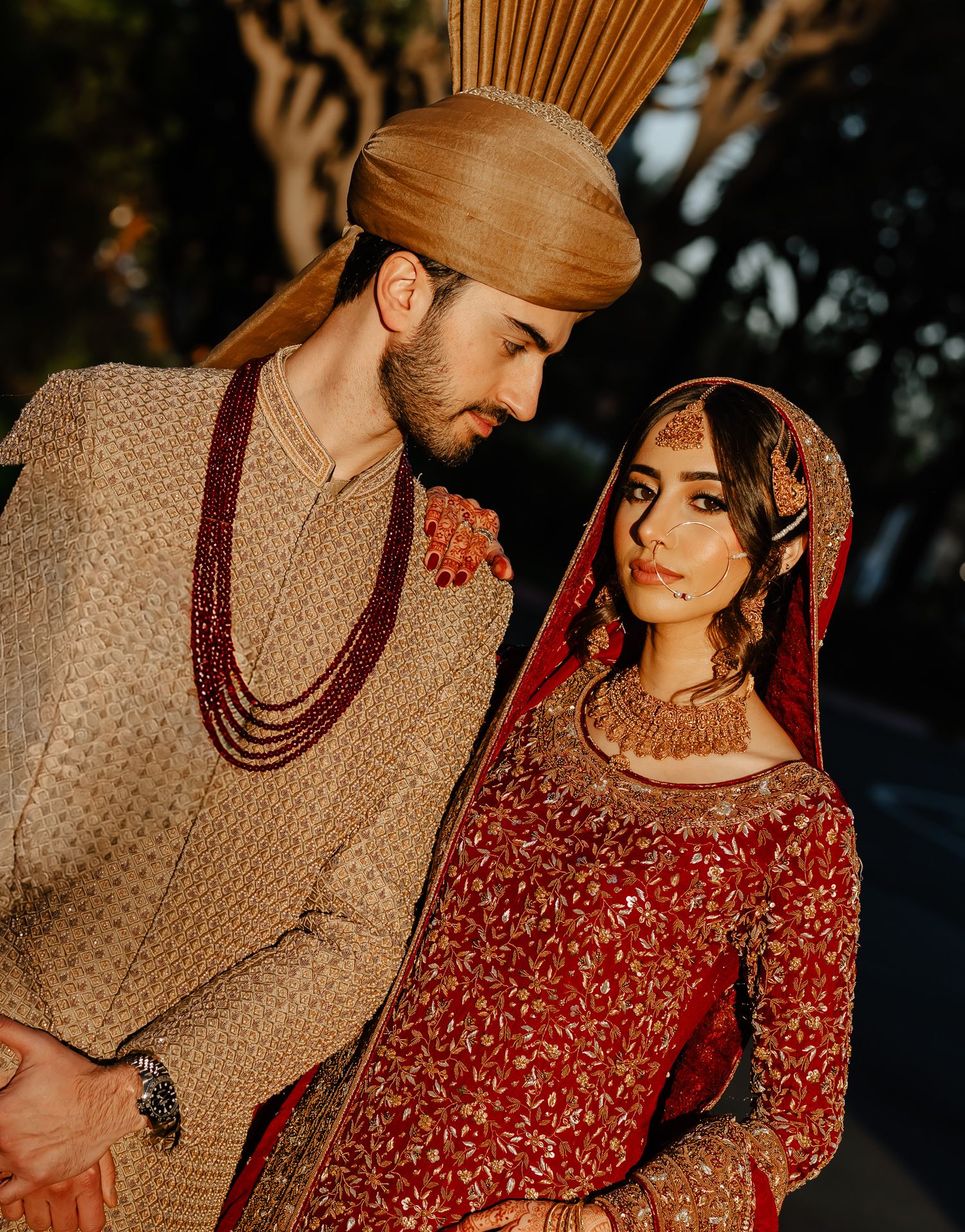 Couple in traditional South Asian wedding attire poses together during golden hour outdoor photoshoot.