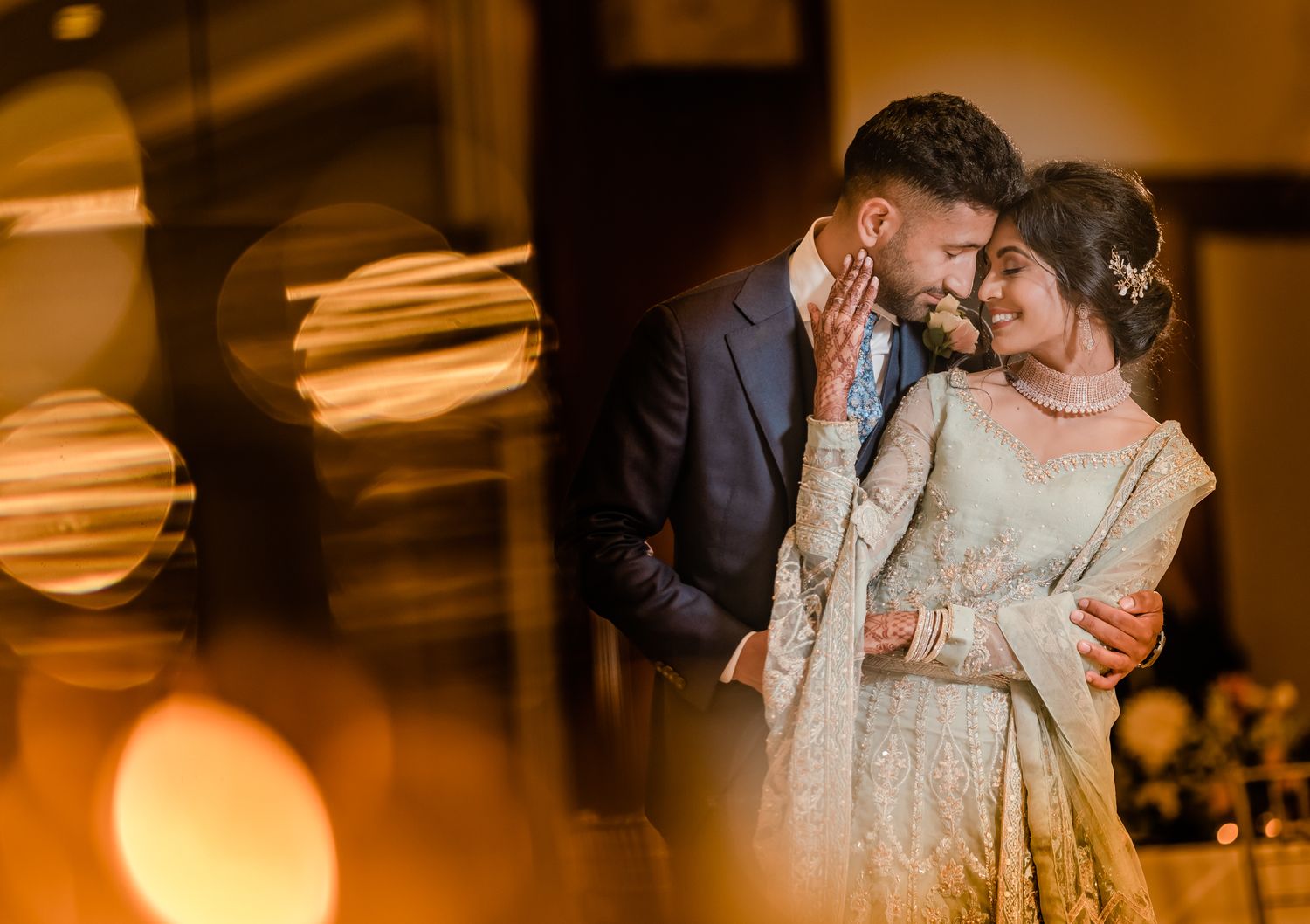 A romantic wedding couple shares an intimate moment on their special day with warm bokeh lighting in the background.