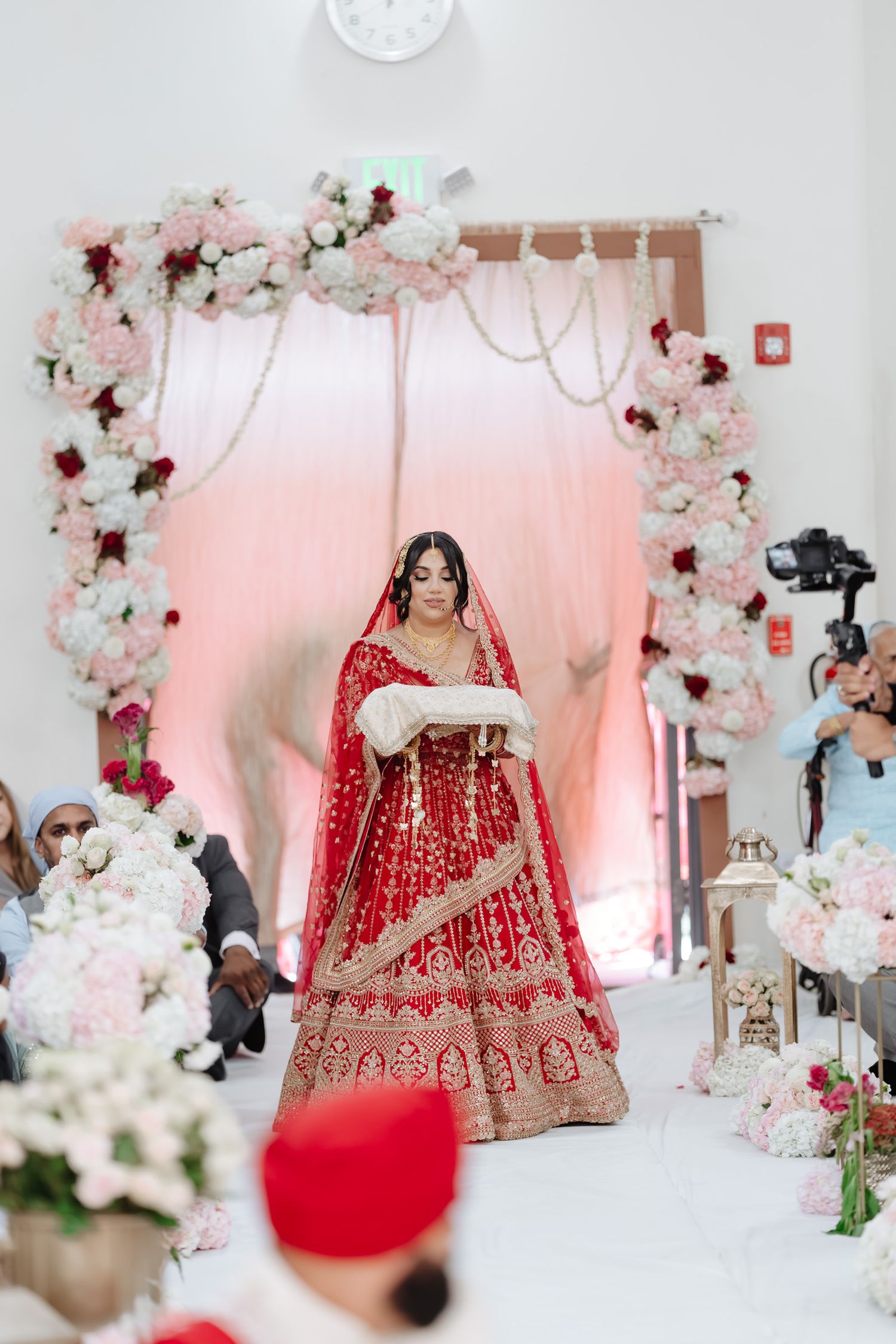 Elegant red and gold Indian bridal lehenga displayed with floral decorations and soft pink lighting.