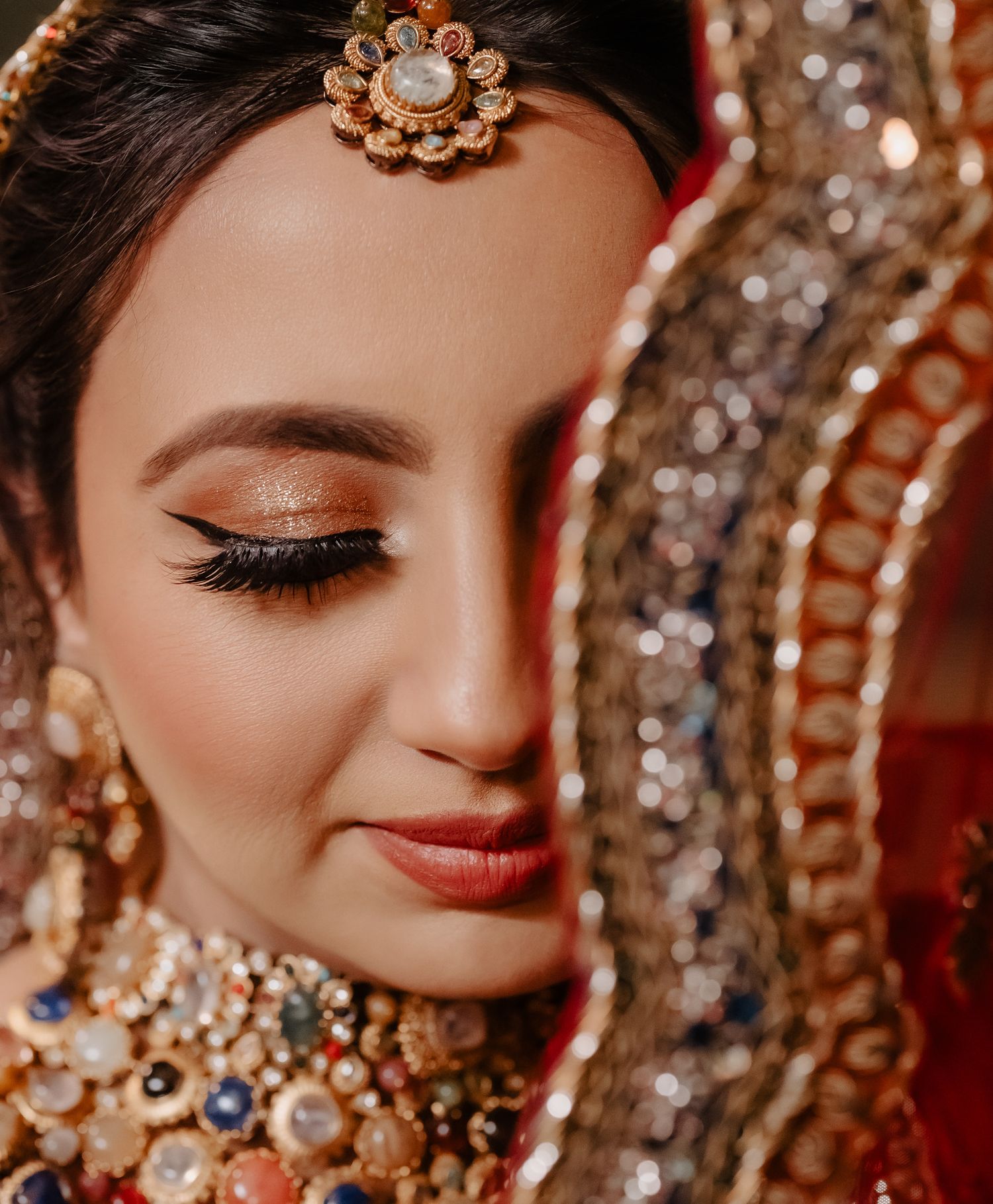 Close-up details of ornate gold and crystal bridal jewelry and makeup in warm tones.