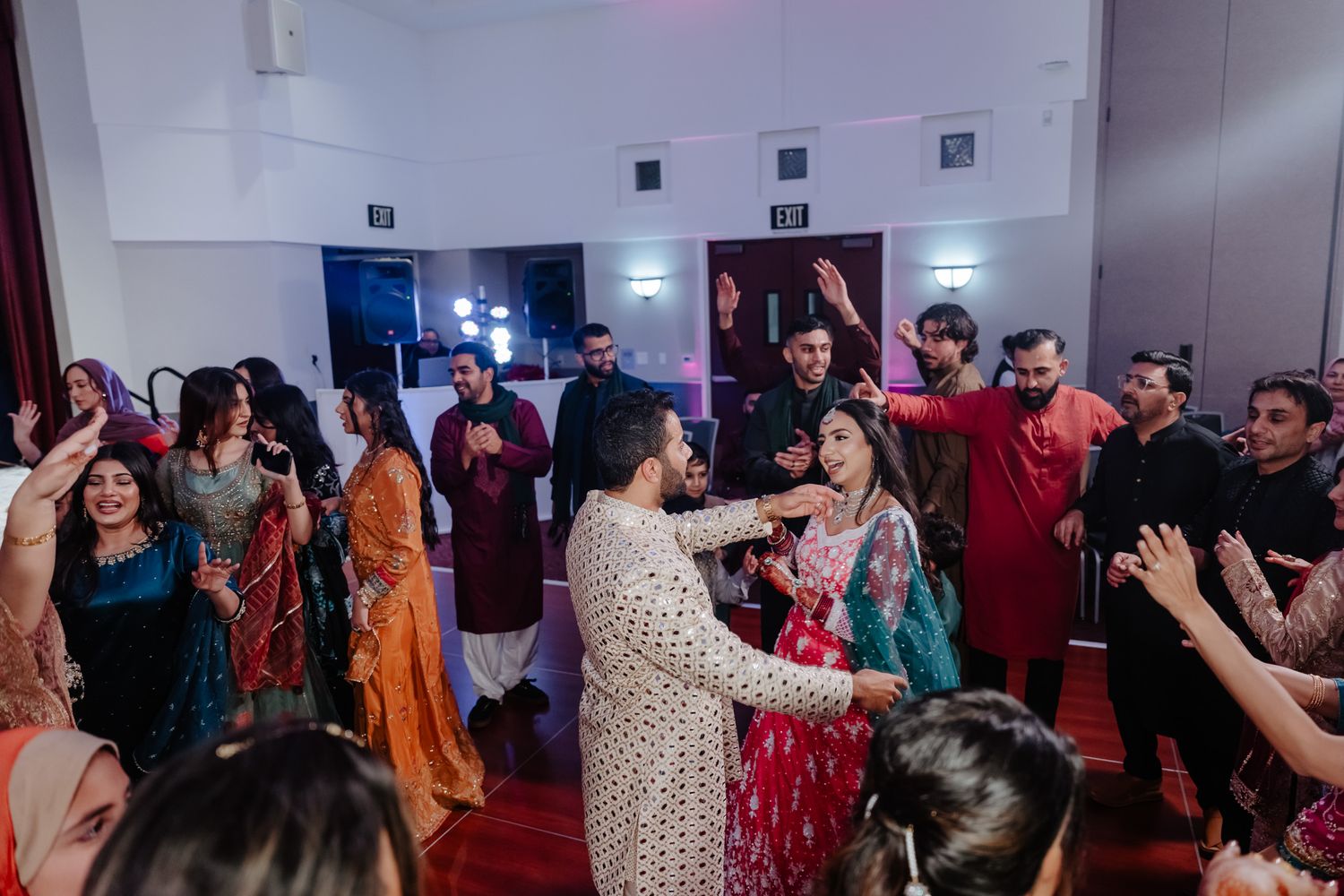 Large group of wedding guests dancing and celebrating in a reception hall with colorful outfits.