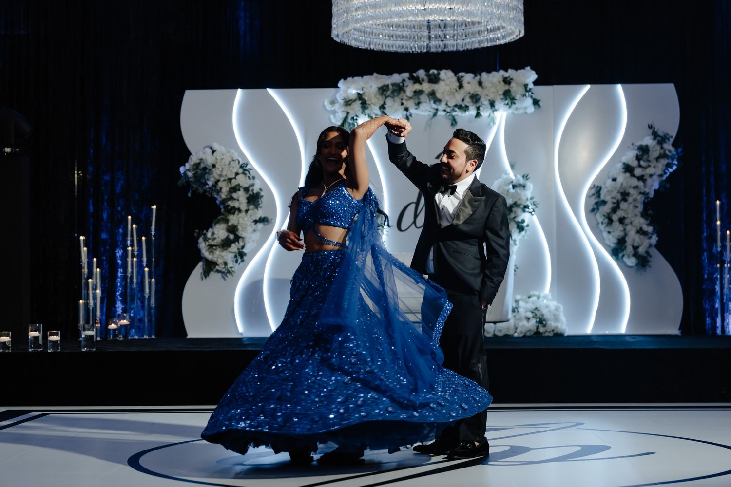 Dancers perform an elegant ballroom dance routine on an illuminated stage with dramatic blue lighting.