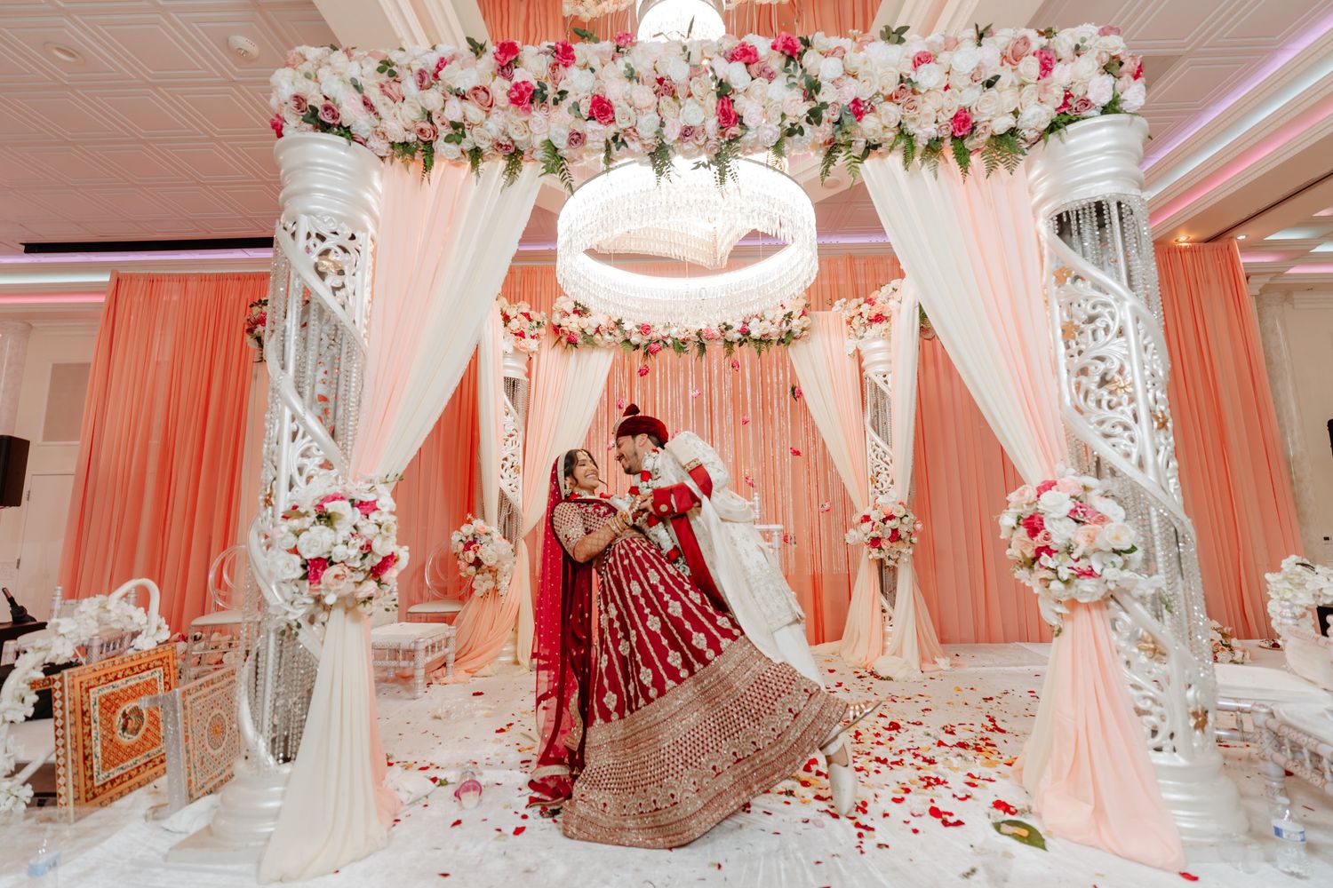 Elegant wedding venue decorated with pink drapes, floral arrangements and crystal chandeliers.