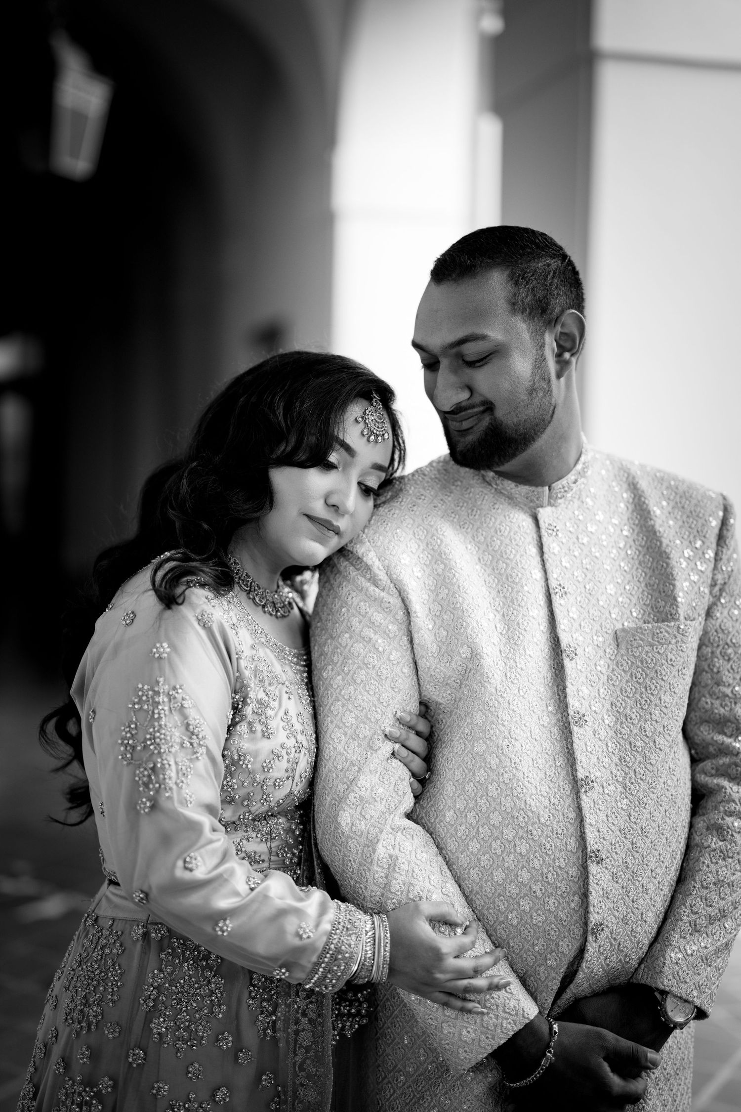 A romantic black and white portrait of a couple in elegant Indian wedding attire sharing an intimate moment.