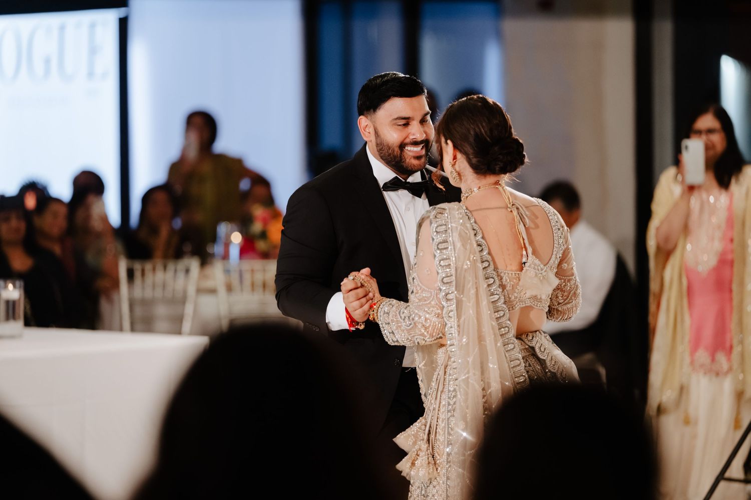 Bride and groom share first dance at elegant wedding reception, bride wearing embroidered saree gown, groom in black tuxedo.
