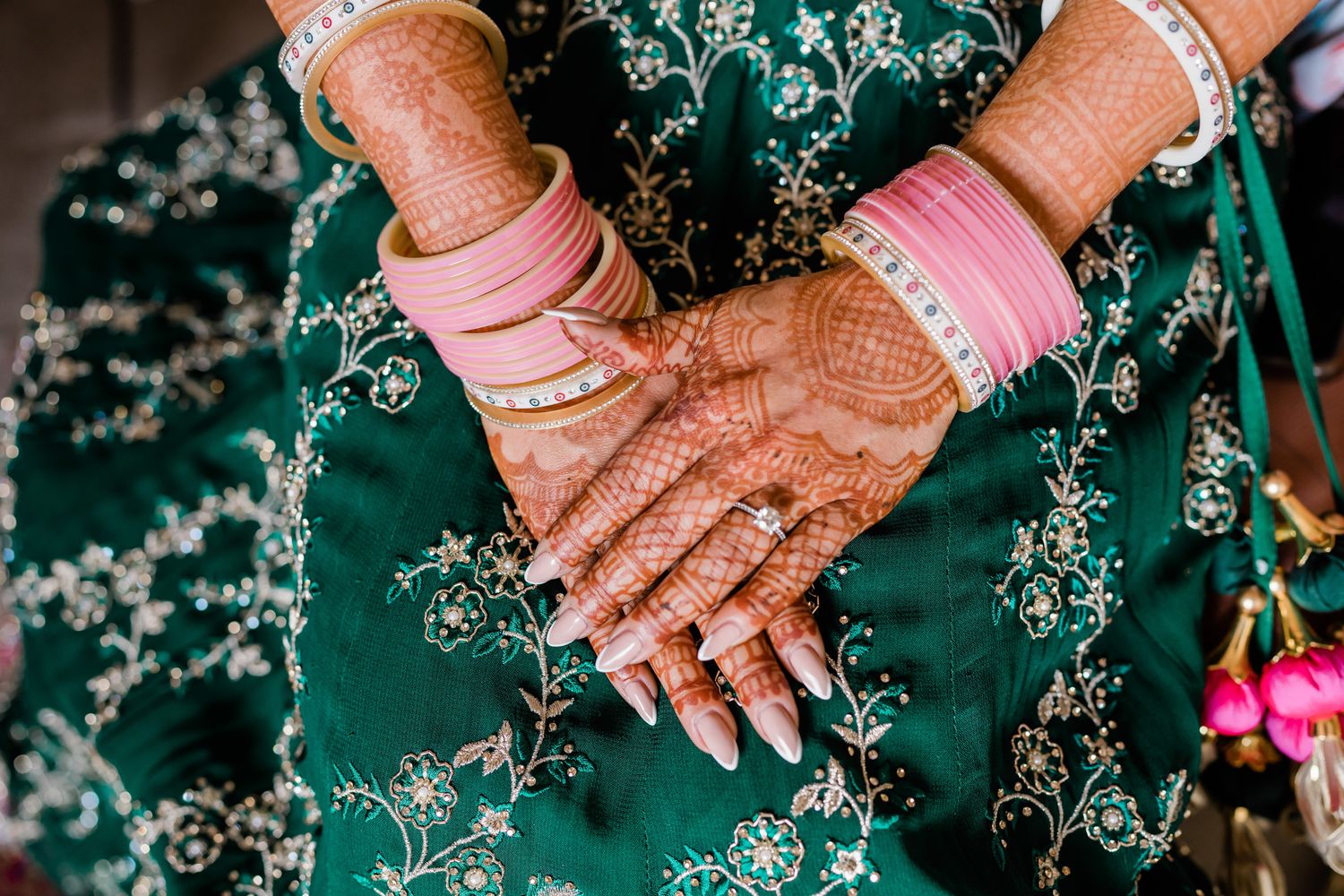 Close-up details of intricate henna designs on hands adorned with jewelry against a teal background.